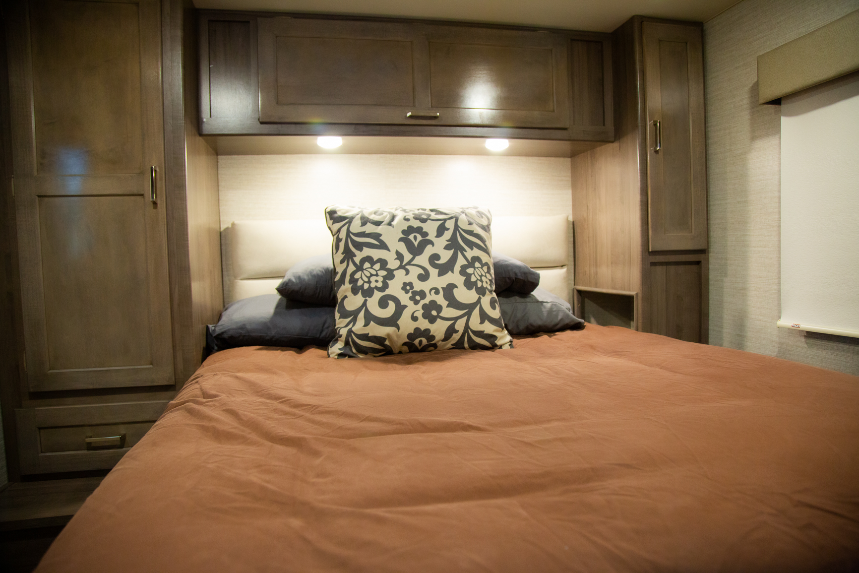 Cozy RV rental bedroom featuring warm brown bedding, a decorative pillow, built-in storage, and ambient lighting.. Winnebago Minnie Winnie 2020