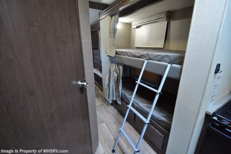 Cozy bunk beds with ladder inside an RV rental, perfect for families. Features include storage and a small kitchen area.. Thor Motor Coach Four Winds 2017