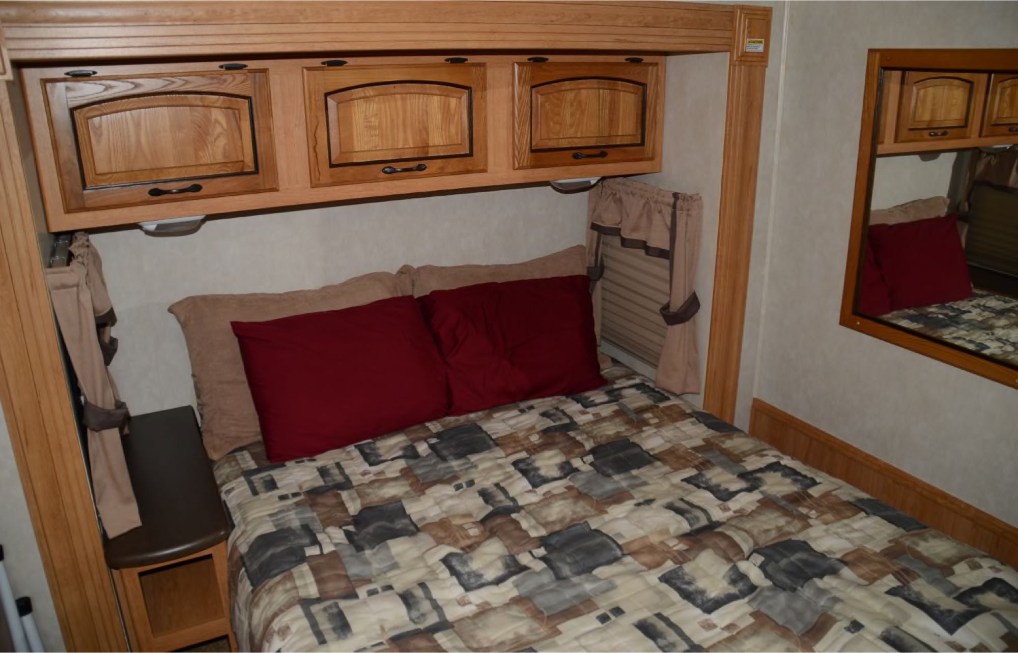 Cozy RV rental bedroom featuring a bed with red pillows, overhead cabinets, and a mirror. Ideal sleeping area.. Coachmen Mirada 2011