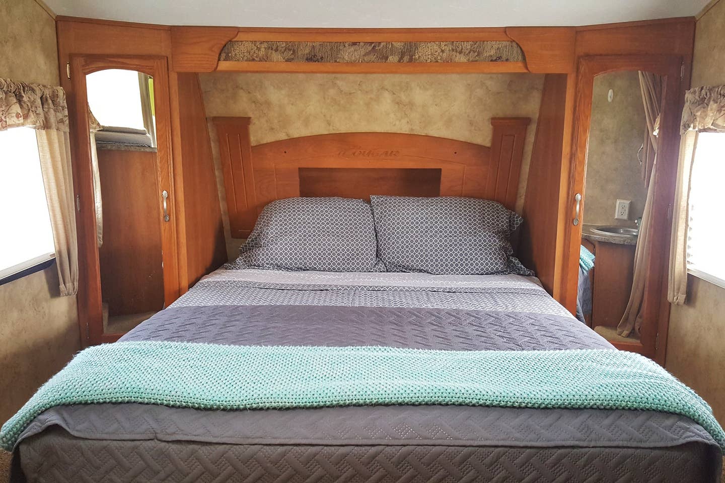 This RV rental bedroom features a patterned bed, teal blanket, wooden built-ins, and a small sink vanity.. Keystone Cougar 2008