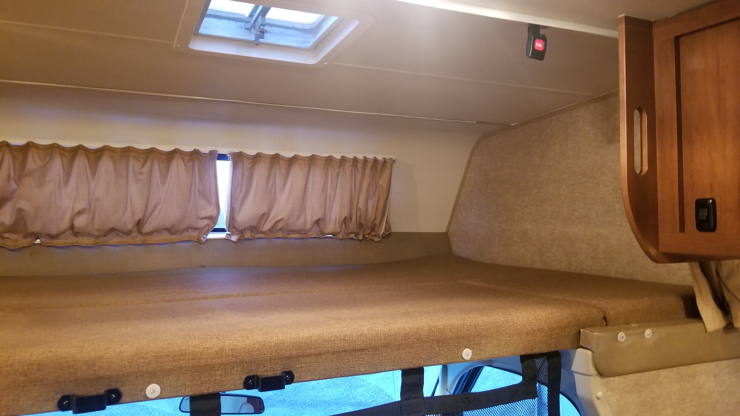 Interior view of an RV rental showing a spacious cab-over bunk bed, with curtains, skylight, and safety net.. Coachmen Leprechaun 2017