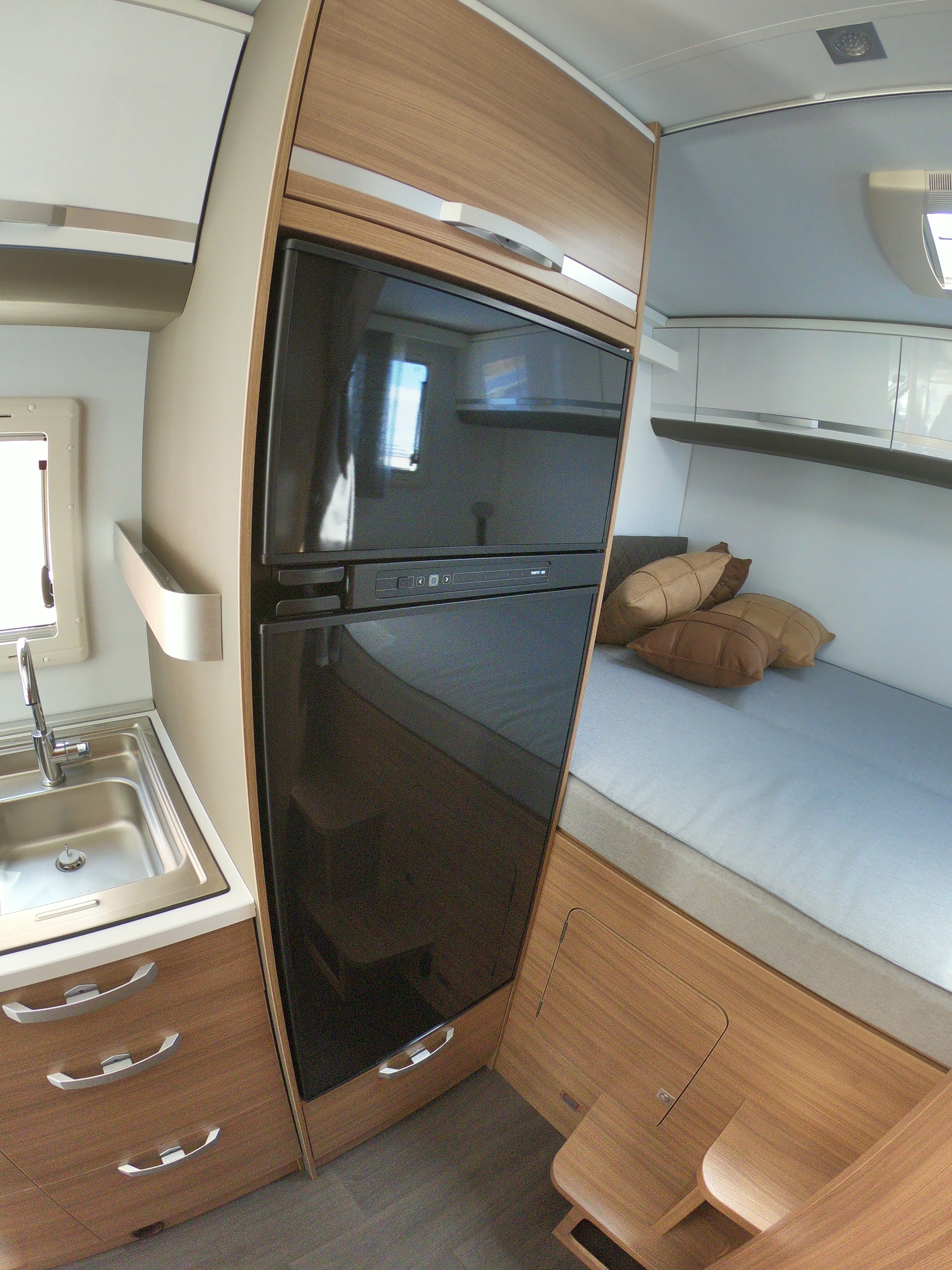 Modern RV rental interior featuring a kitchen sink, large refrigerator, and cozy bed area.. Adria Coral 600 DP 2020