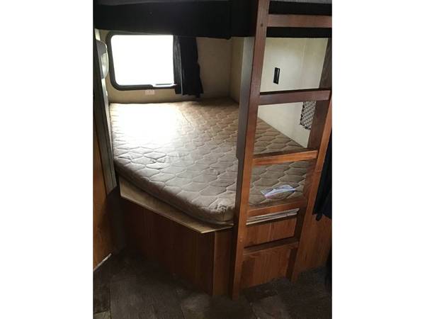 This RV rental features a cozy bunk bed setup: a lower bed with a quilted mattress, a window, and a wooden ladder for the upper bunk.. Starcraft 27bhs 2017
