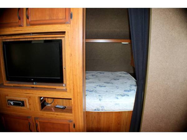 RV rental interior: wooden entertainment center with TV, stereo, and media devices, plus a bunk bed with curtain.. Starcraft 27bhs 2017