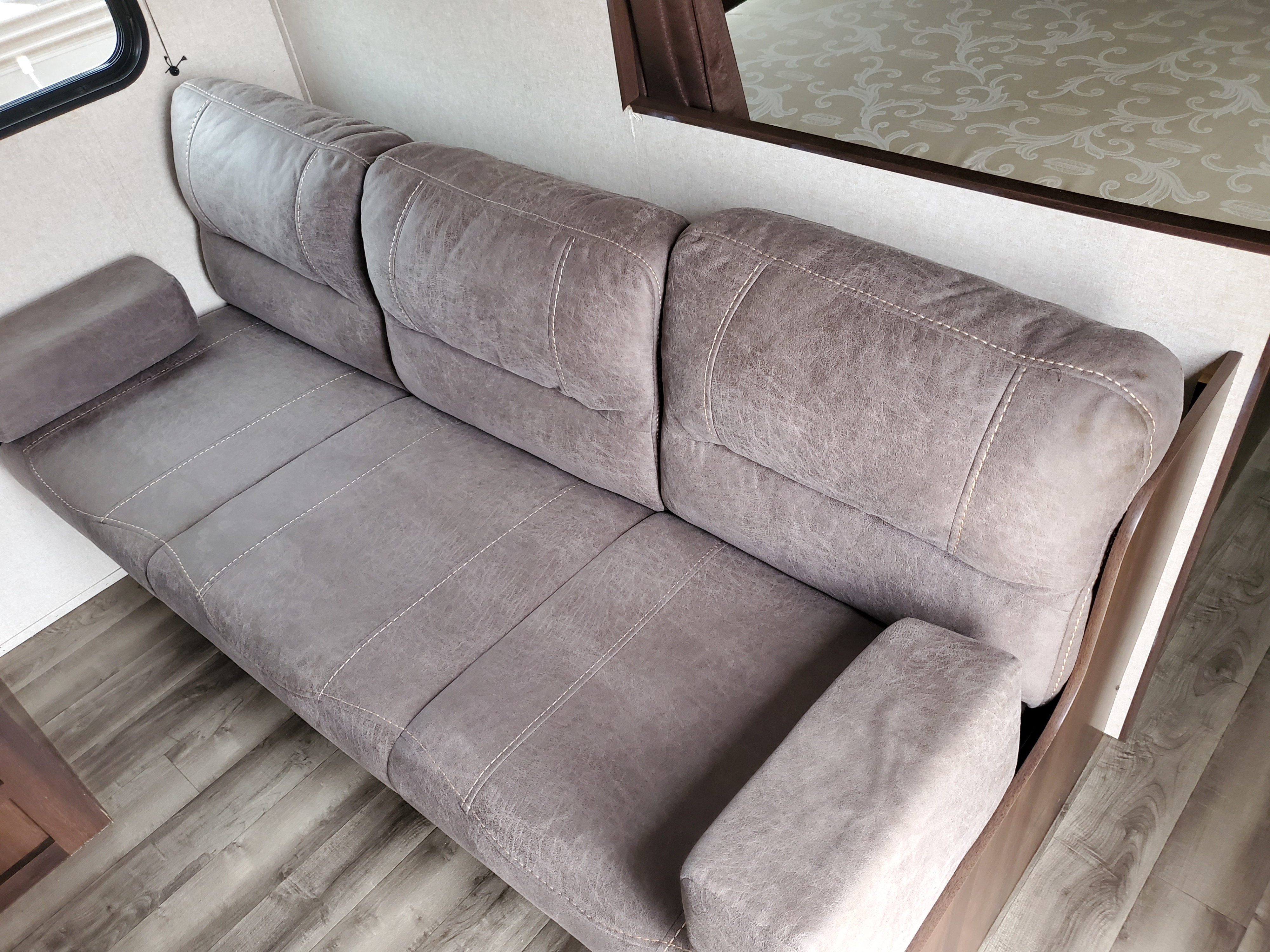 A plush gray sofa with prominent stitching in a modern RV rental, featuring durable-looking upholstery and wood flooring.. Jayco for rent NEW 2019 Jayco 26 foot bunkhouse Rental sleeps 10 2019