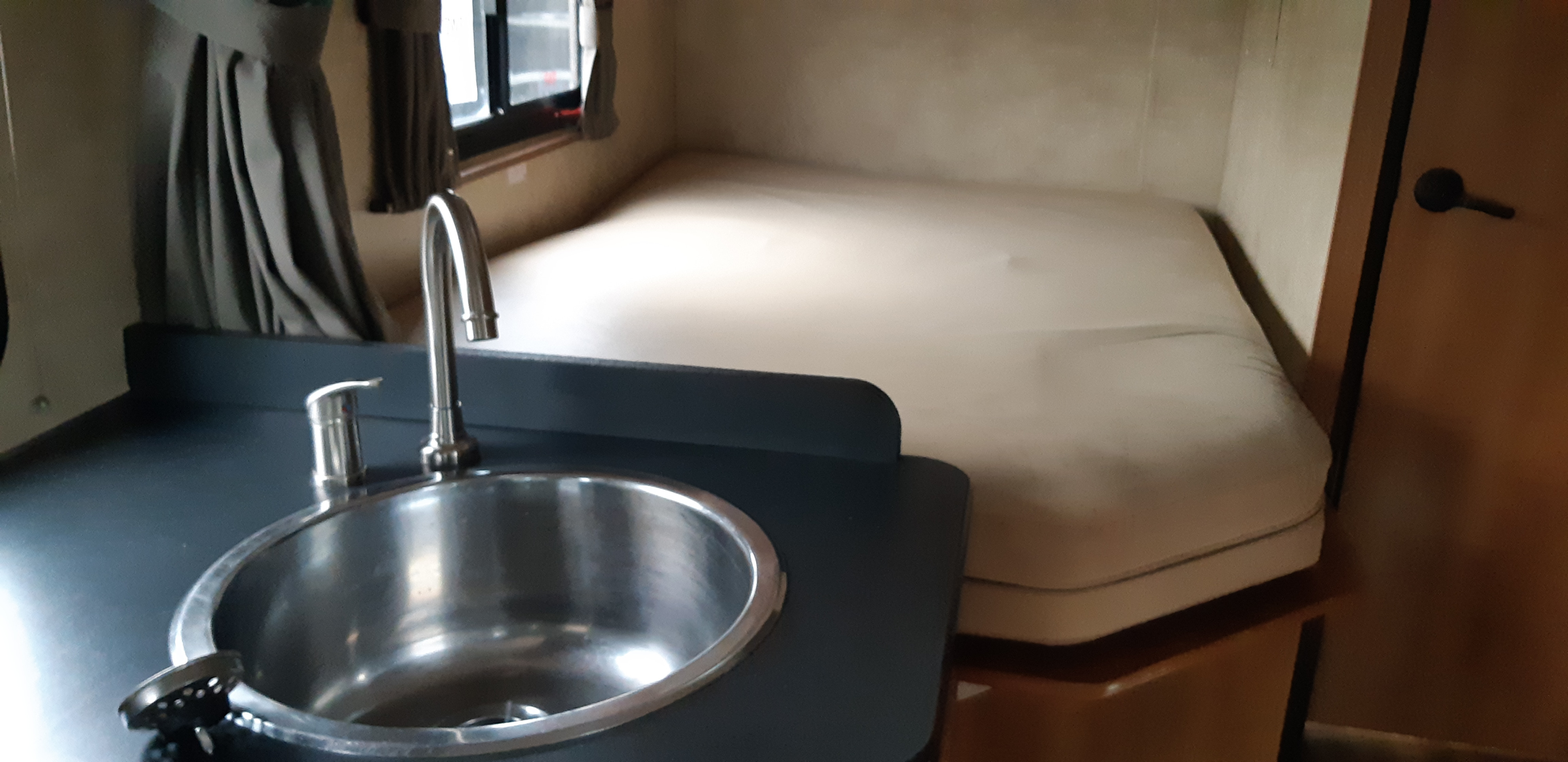 RV rental interior: compact kitchen sink and bed area with window and door, showing a functional small living space.. Thor Majestic 2016