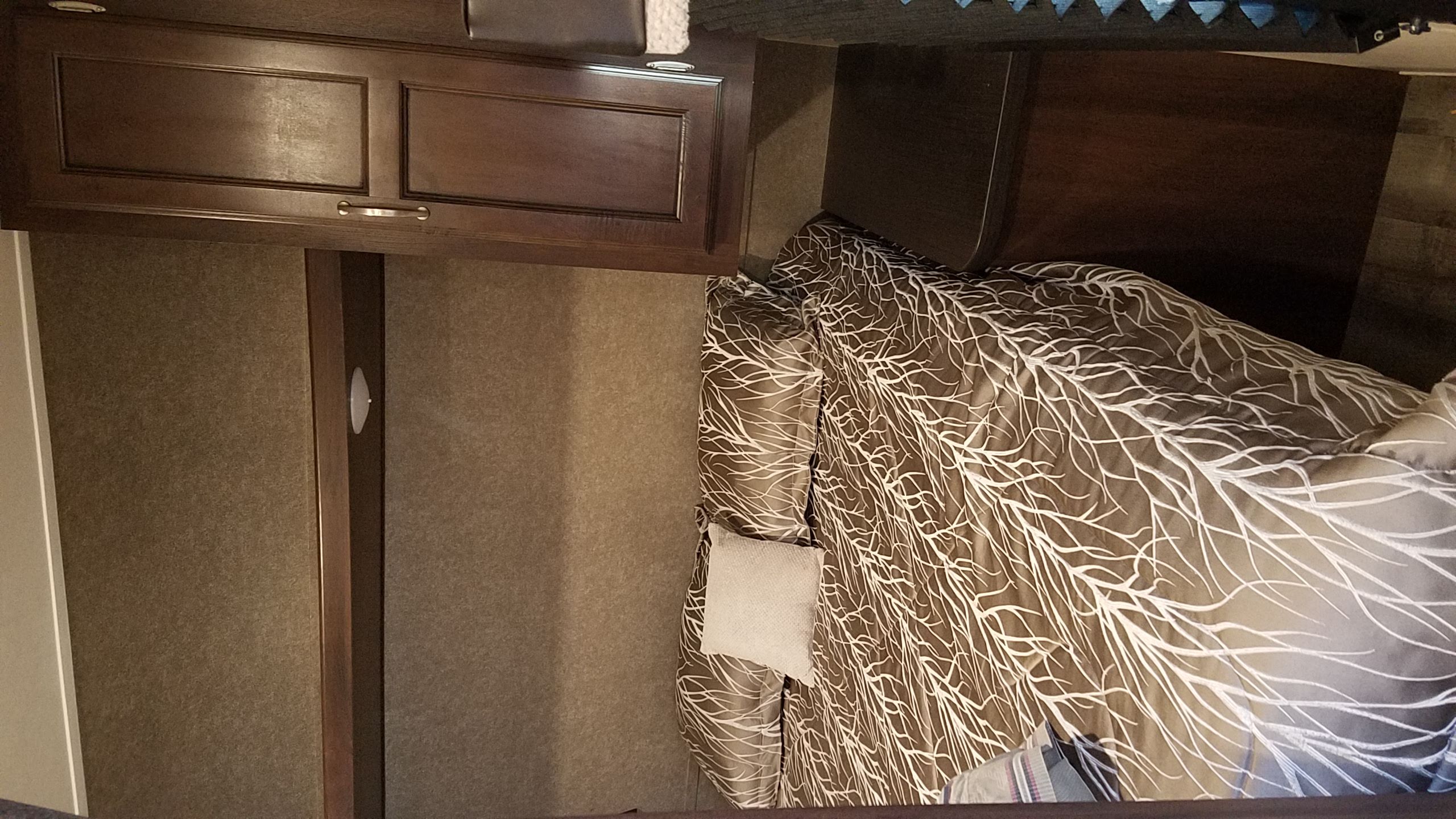 RV rental bedroom interior featuring a patterned comforter on the bed, dark wood cabinets, and fabric walls.. Jayco Jay Flight SLX 2018