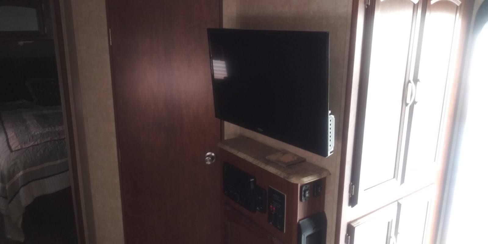 RV rental interior featuring a wall-mounted TV, entertainment system, and bedroom doorway with a glimpse of the bed.. Forest River Heritage Glen 2016