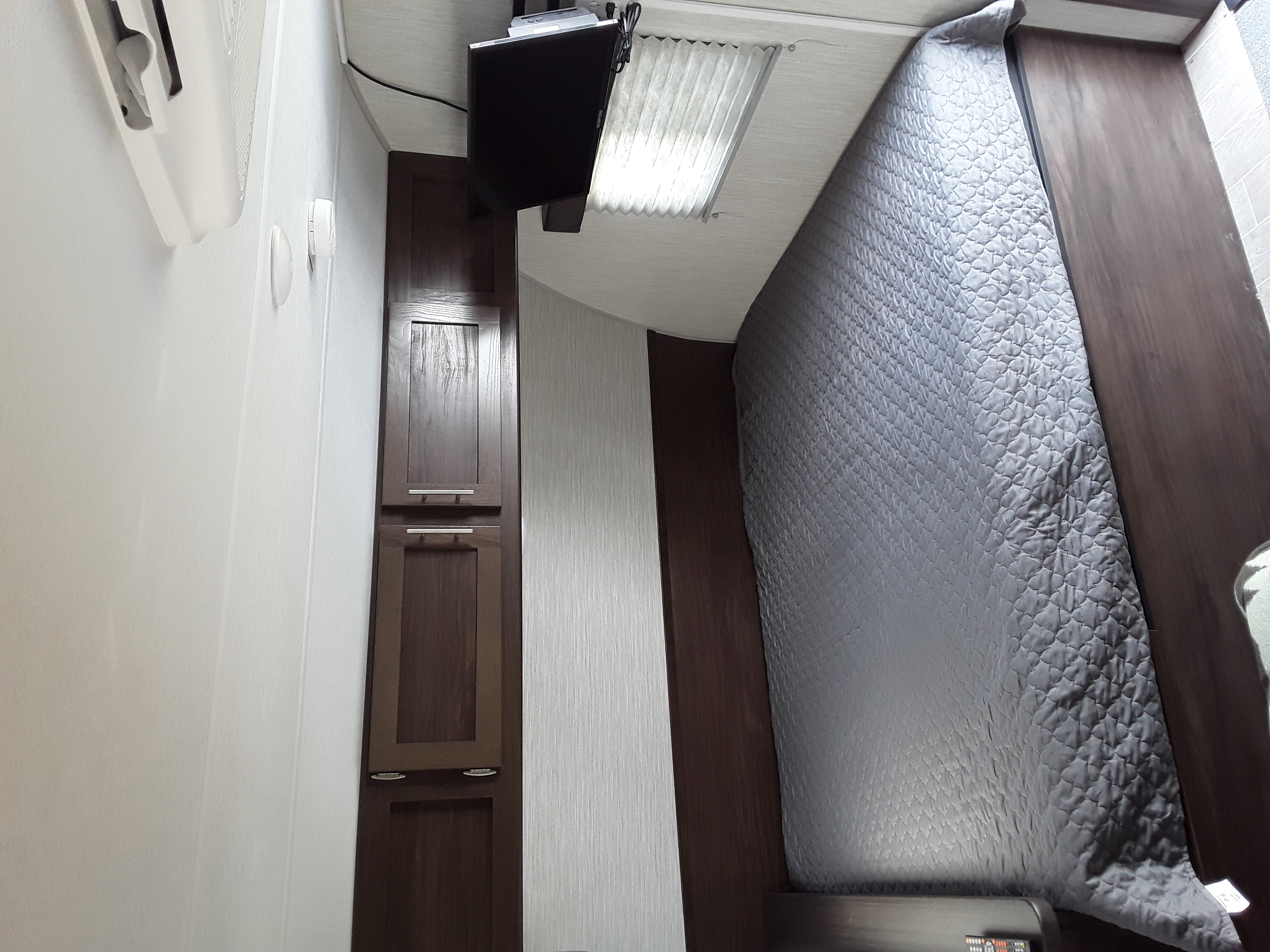 Cozy RV rental bedroom featuring a grey quilted comforter, dark cabinets, and a wall-mounted TV for comfortable travel.. Forest River Wolf Pup 2020