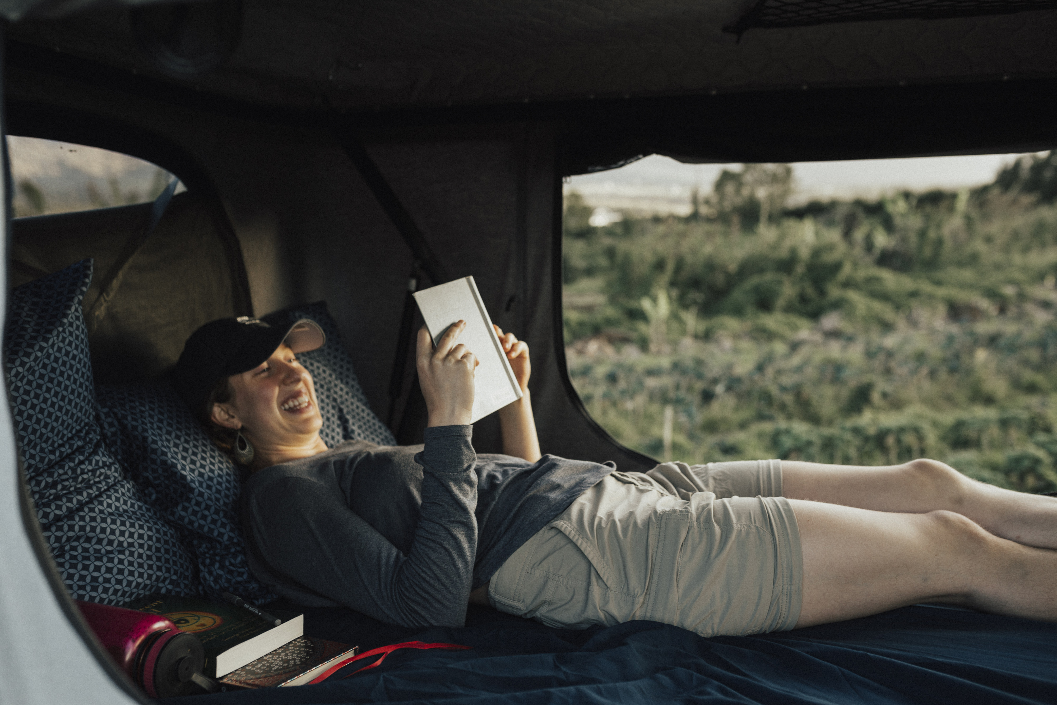 Enjoying a cozy moment inside an RV rental's rooftop tent, a woman relaxes while reading amidst nature.. Nissan Pathfinder 2016
