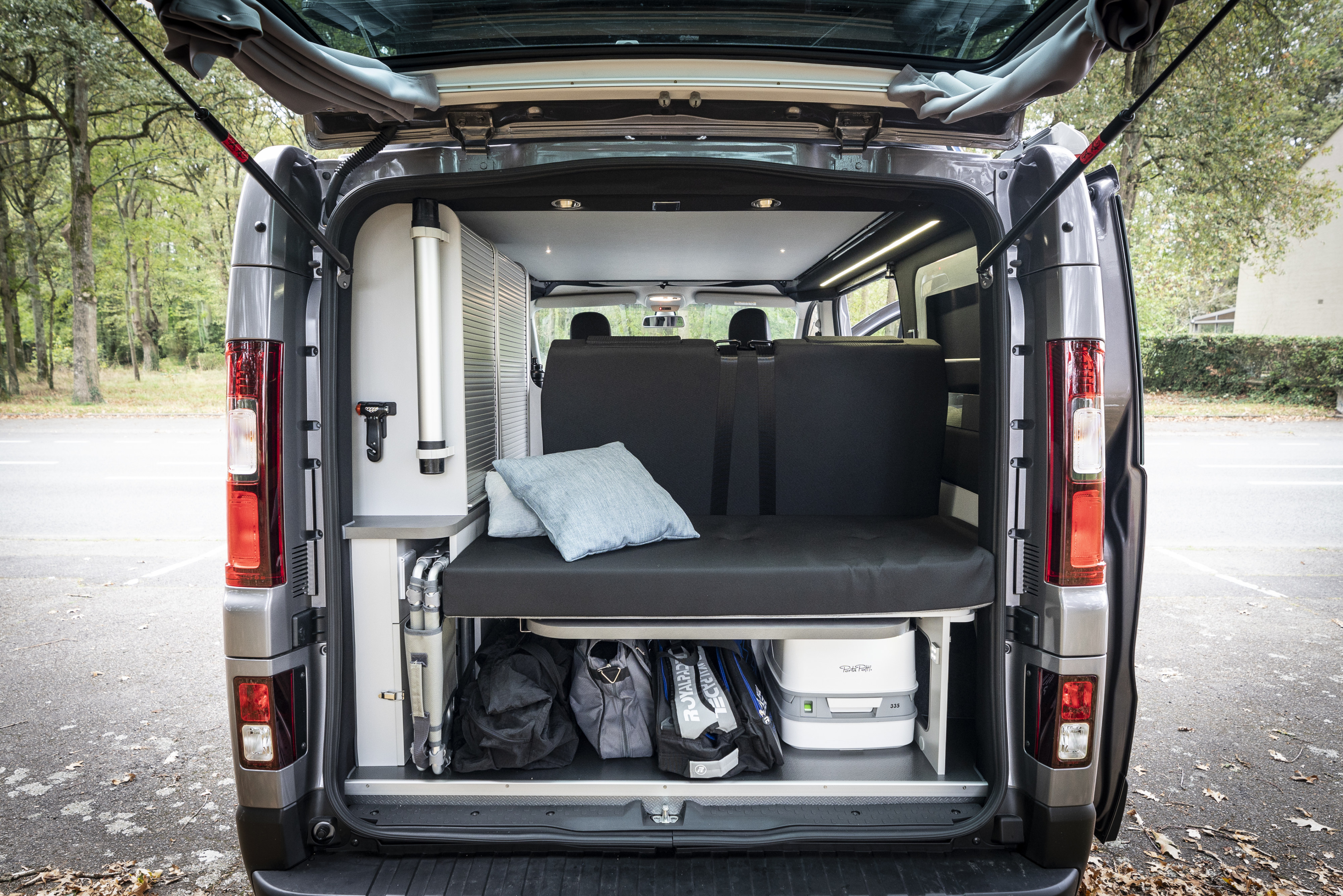 A grey RV rental's rear interior features a bench bed with pillows, under-bed storage, and a portable toilet.. Hanroad Trek 2025