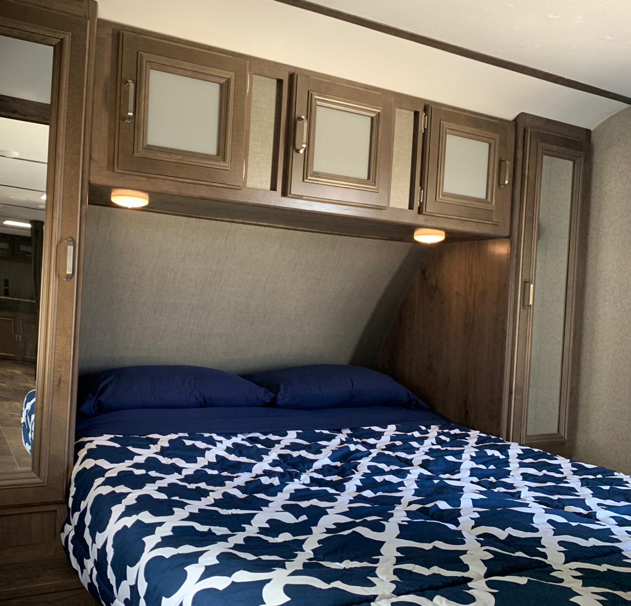 RV rental bedroom: a cozy space with patterned bedding, overhead storage, and warm lighting.. Keystone Passport 2019