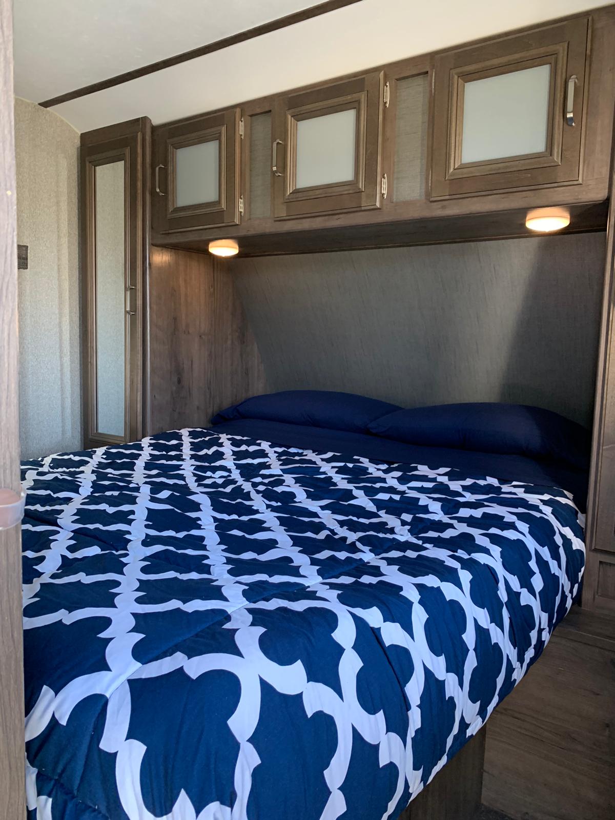 Modern RV rental bedroom: comfy bed, overhead storage, mirrored wardrobe. Ideal for travel & adventures.. Keystone Passport 2019