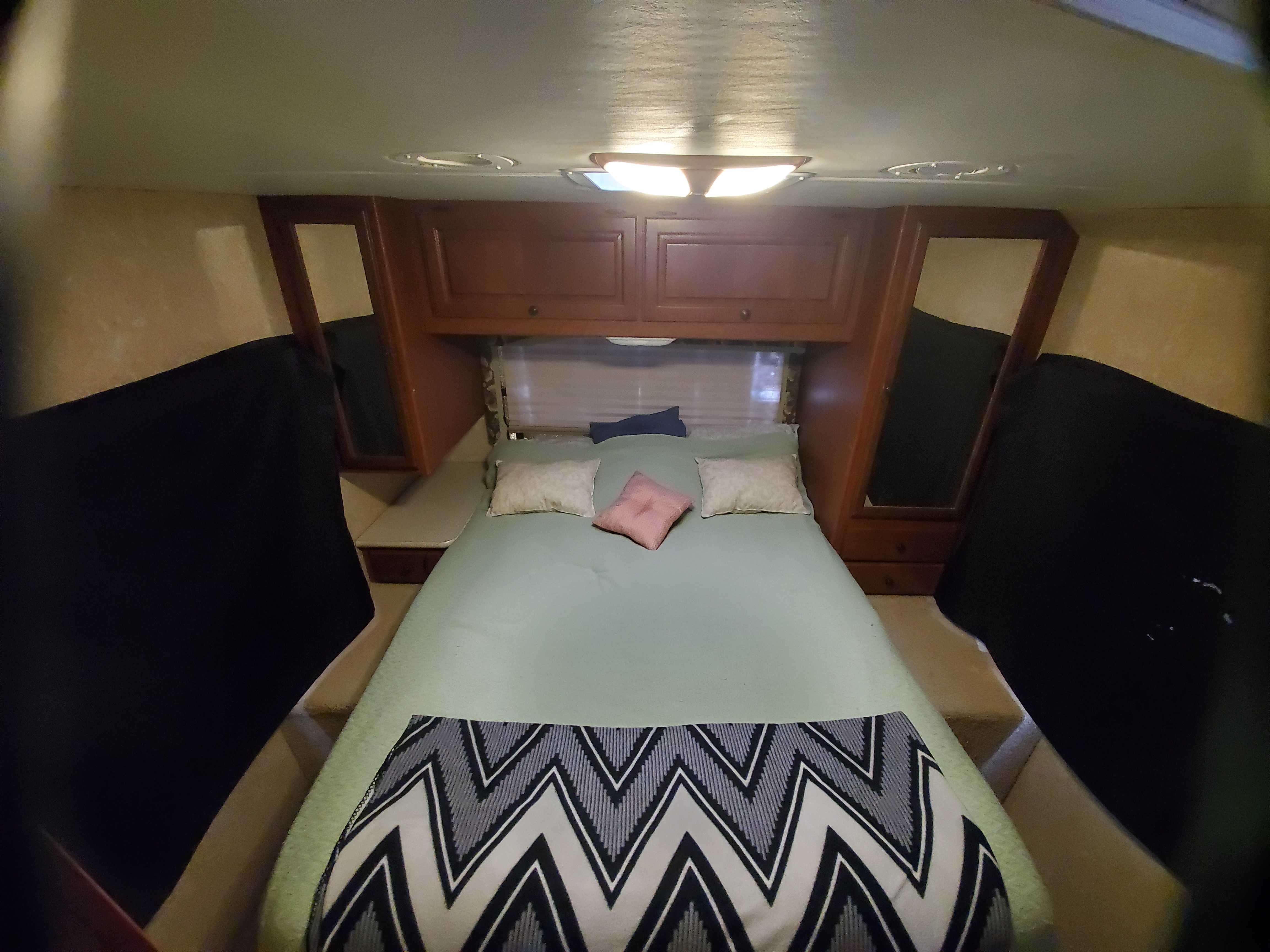 Cozy RV rental bedroom with light green bedding, a patterned blanket, and built-in cabinets, offering a comfortable sleeping area.. Ford Fourwinds 2012