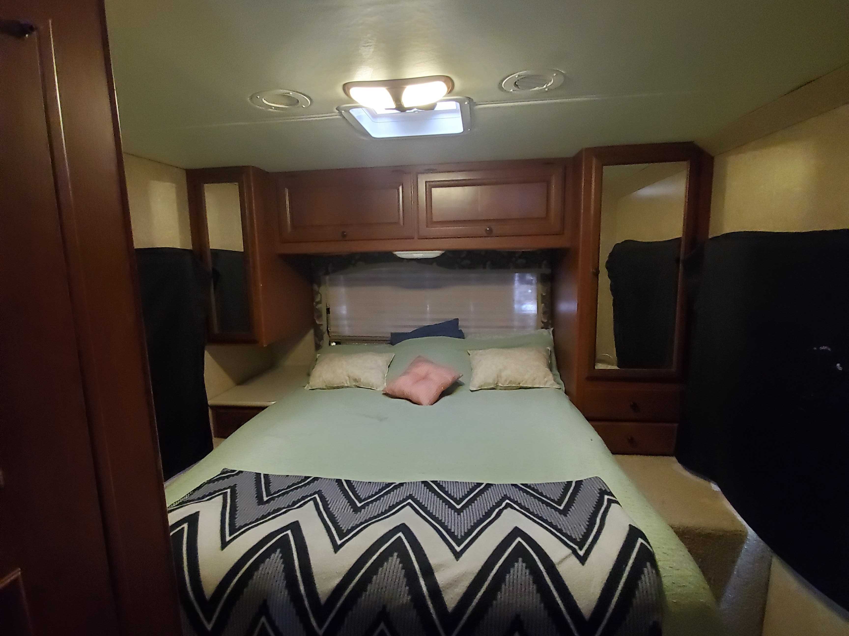 Cozy RV rental bedroom featuring a comfortable bed, overhead cabinets, and clever built-in storage. Ideal for travel.. Ford Fourwinds 2012