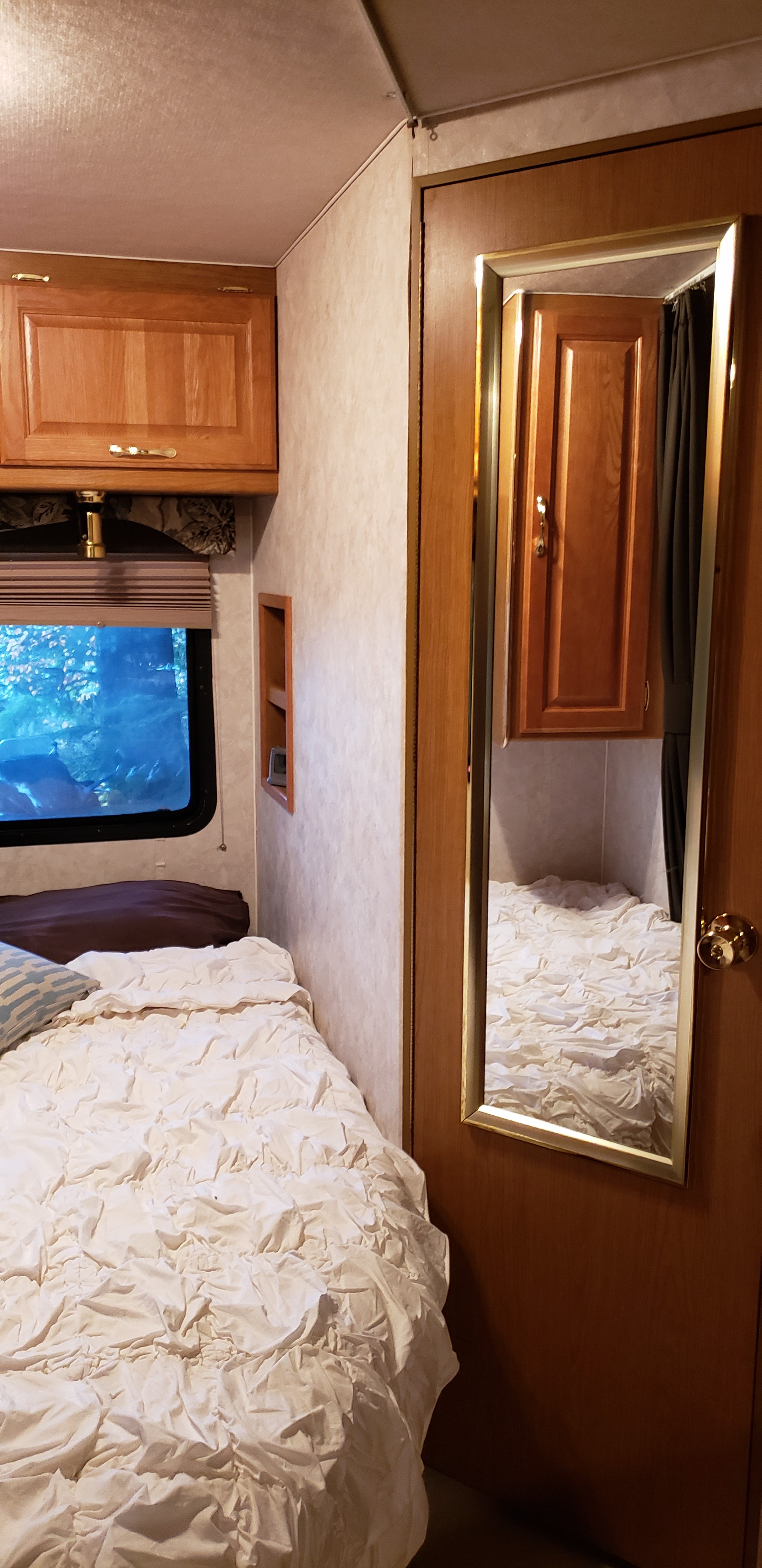 Cozy RV rental bedroom with a bed, outdoor window view, wooden cabinet, and a mirrored door.. Triple E Senator 2000