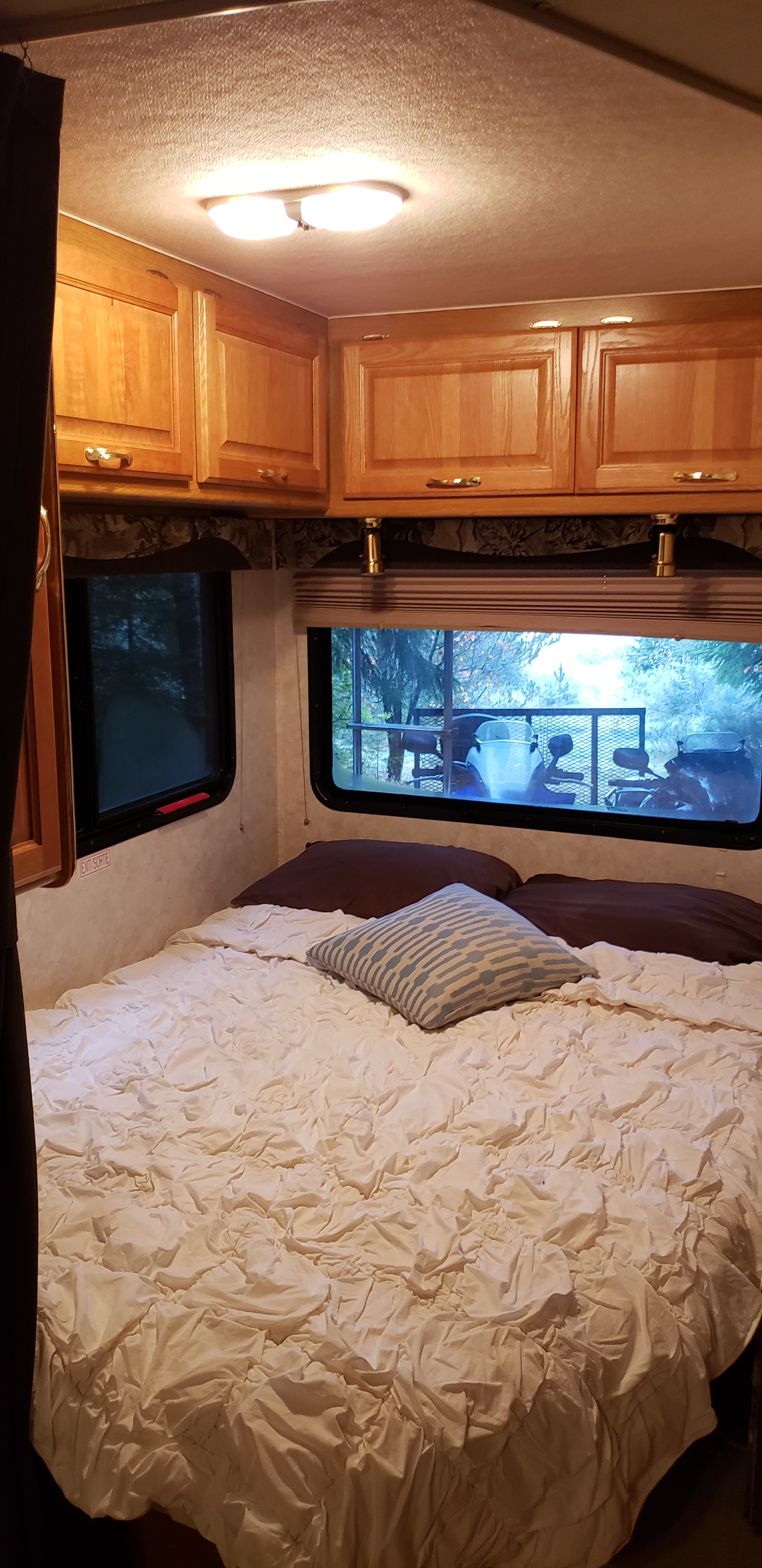 Cozy RV bedroom with ruffled bed, wood cabinets, and outdoor views through windows—ideal for an RV rental experience.. Triple E Senator 2000
