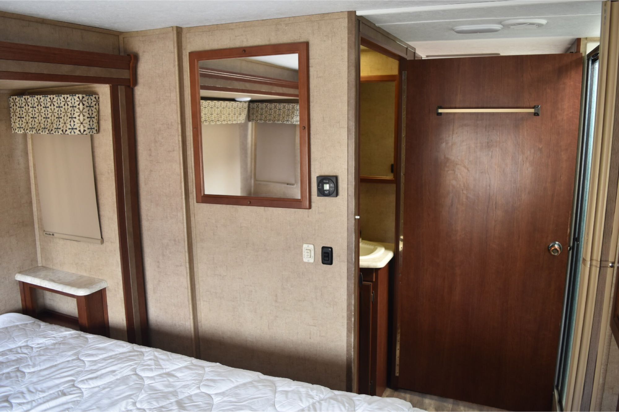 This RV rental shows a compact bedroom with a connected bathroom. Features include a bed, mirror, and climate controls for comfortable mobile living.. Forest River Sunseeker 2017