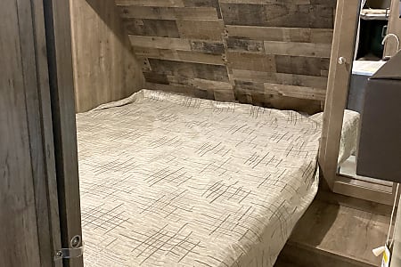 Interior of an RV rental: a cozy bedroom with a bed featuring a light patterned comforter and wood-paneled walls.. Dutchmen Aspen Trail 2020