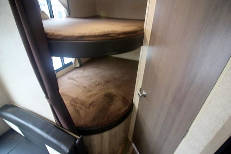 Inside an RV rental, showing a compact sleeping area with two brown bunk beds and a brown privacy curtain.. Coachmen Catalina 2019
