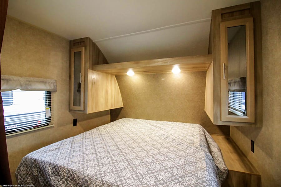 An RV rental's compact bedroom with a patterned bed, overhead lights, and built-in storage cabinets.. Coachmen Catalina 2019