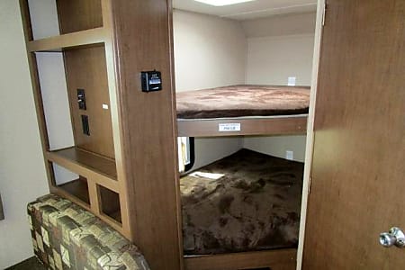Comfortable RV rental interior with two cozy bunk beds, brown bedding, and a storage unit. Ideal for family travel.. Shasta Oasis 2018