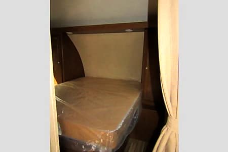 RV rental interior: a clean bedroom with a bed, its mattress covered in protective plastic, and wood-toned cabinetry.. Shasta Oasis 2018