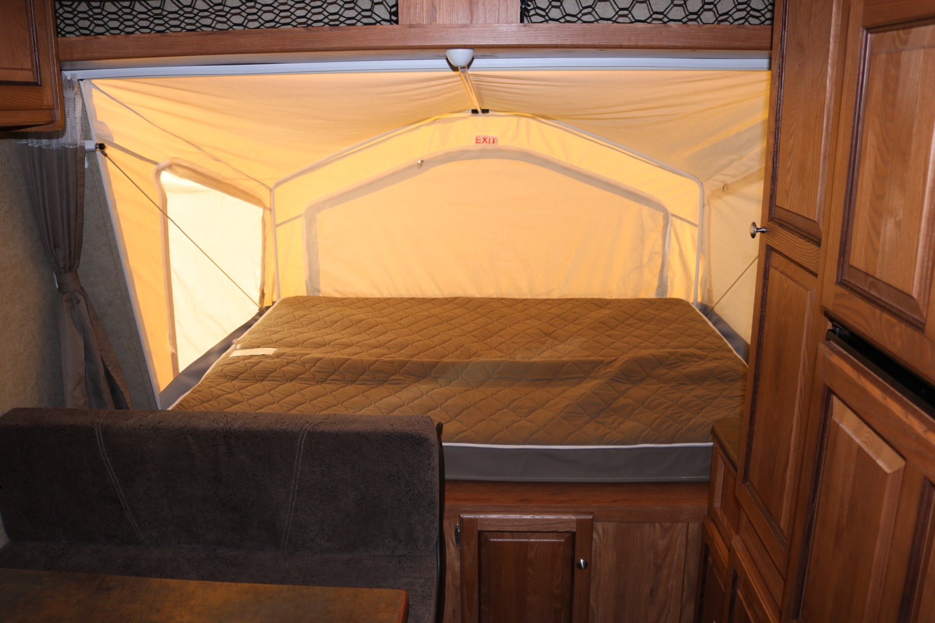 Inside an RV rental: a large, comfortable bed in a light yellow pop-out tent extension, with dark wood cabinets and a sofa.. Forest River Rockwood Roo 17 2016