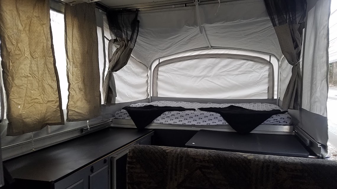 Interior of a cozy RV rental pop-up camper. Features a comfortable bed, practical counters, and adjustable curtains for privacy.. Fleetwood Evolution 2007