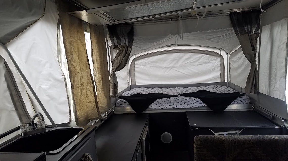 Inside an rv rental pop-up camper, featuring a bed, small kitchen sink, and versatile living space.. Fleetwood Evolution 2007