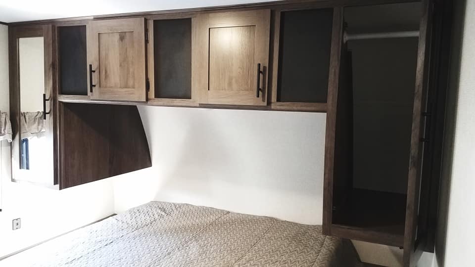 RV rental bedroom featuring a patterned bed, dark wood overhead cabinets with light doors, and an open closet.. Prime Time Avenger 2020