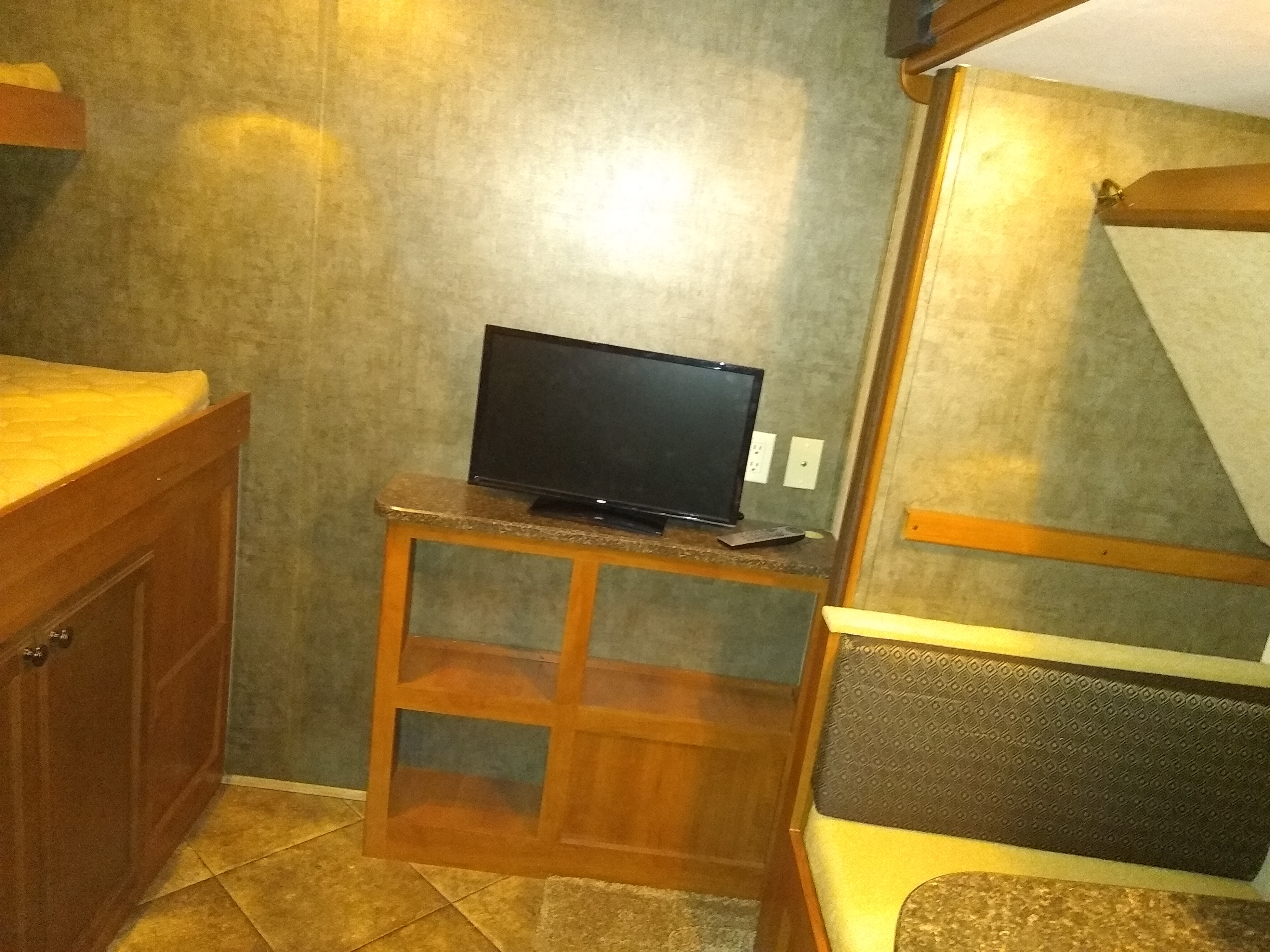 Cozy RV rental interior: bunk bed, TV on a wooden stand, and dining booth with patterned cushions.. Heartland North Trail 2014