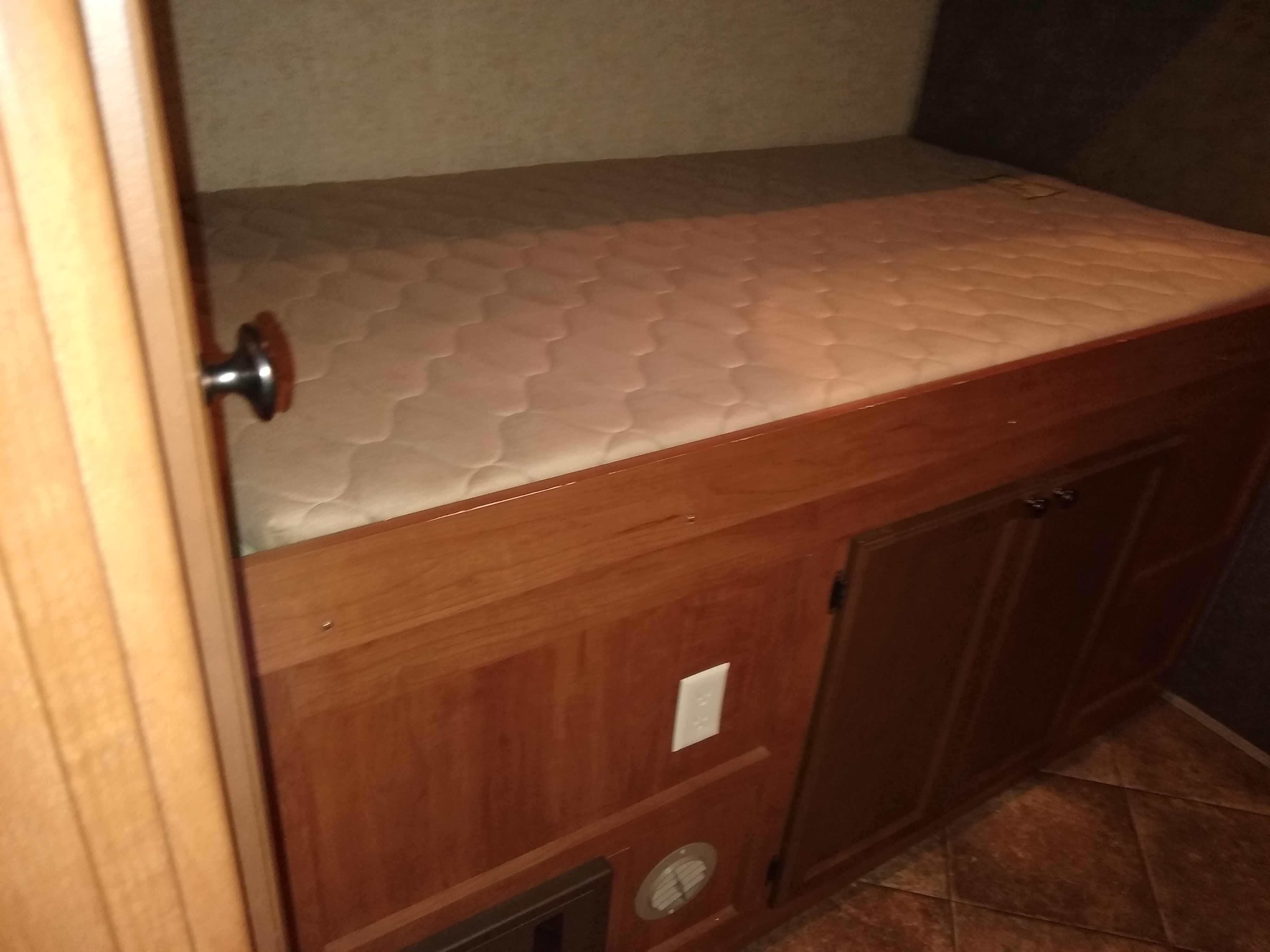 RV rental sleeping area: a compact bed with quilted mattress, built-in wooden storage cabinets, outlet, and floor vent.. Heartland North Trail 2014