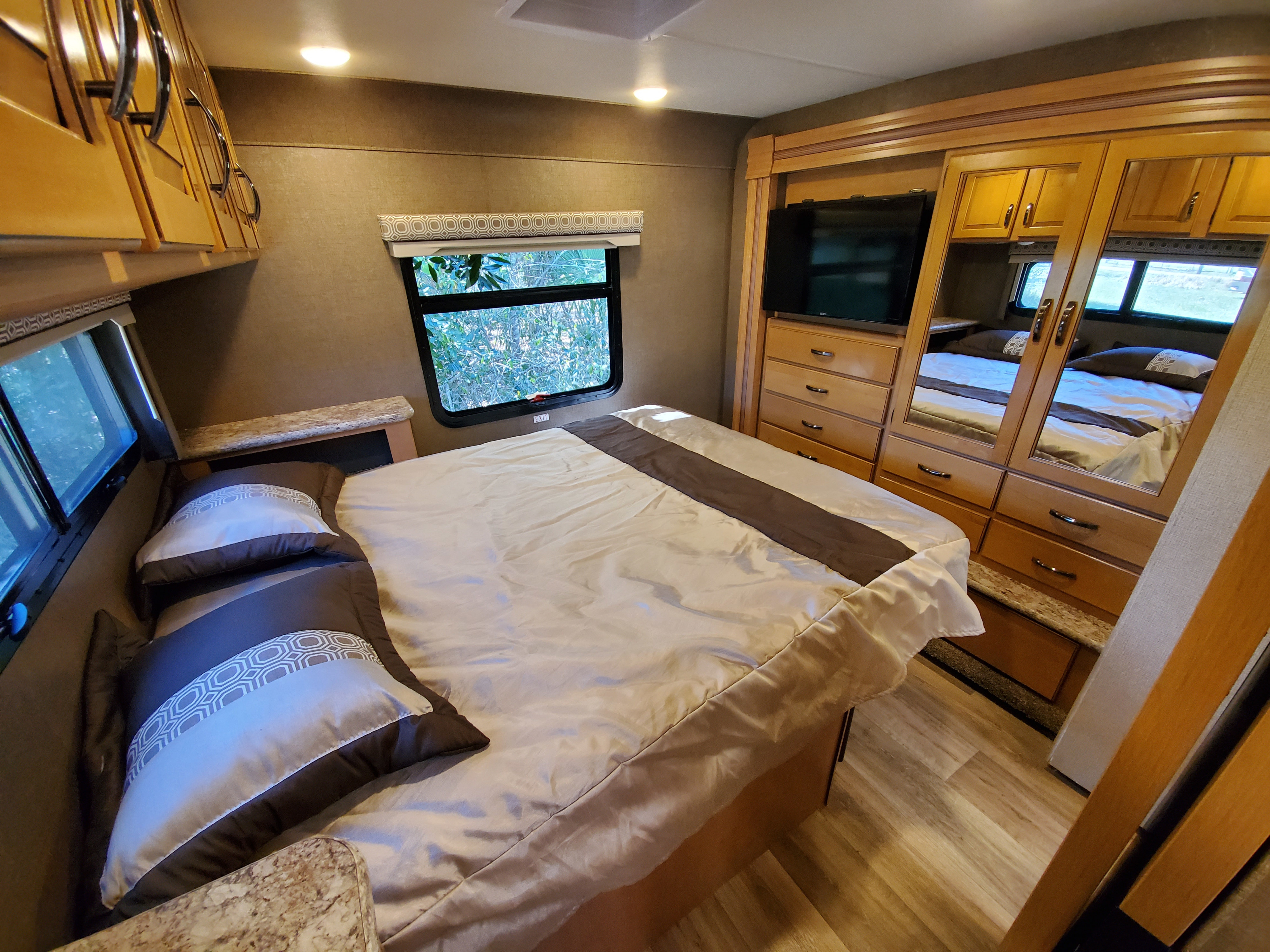 Experience comfort in this modern RV rental bedroom. Features include a cozy bed, TV, and elegant wood cabinetry.. Thor Motor Coach FourWinds 2017