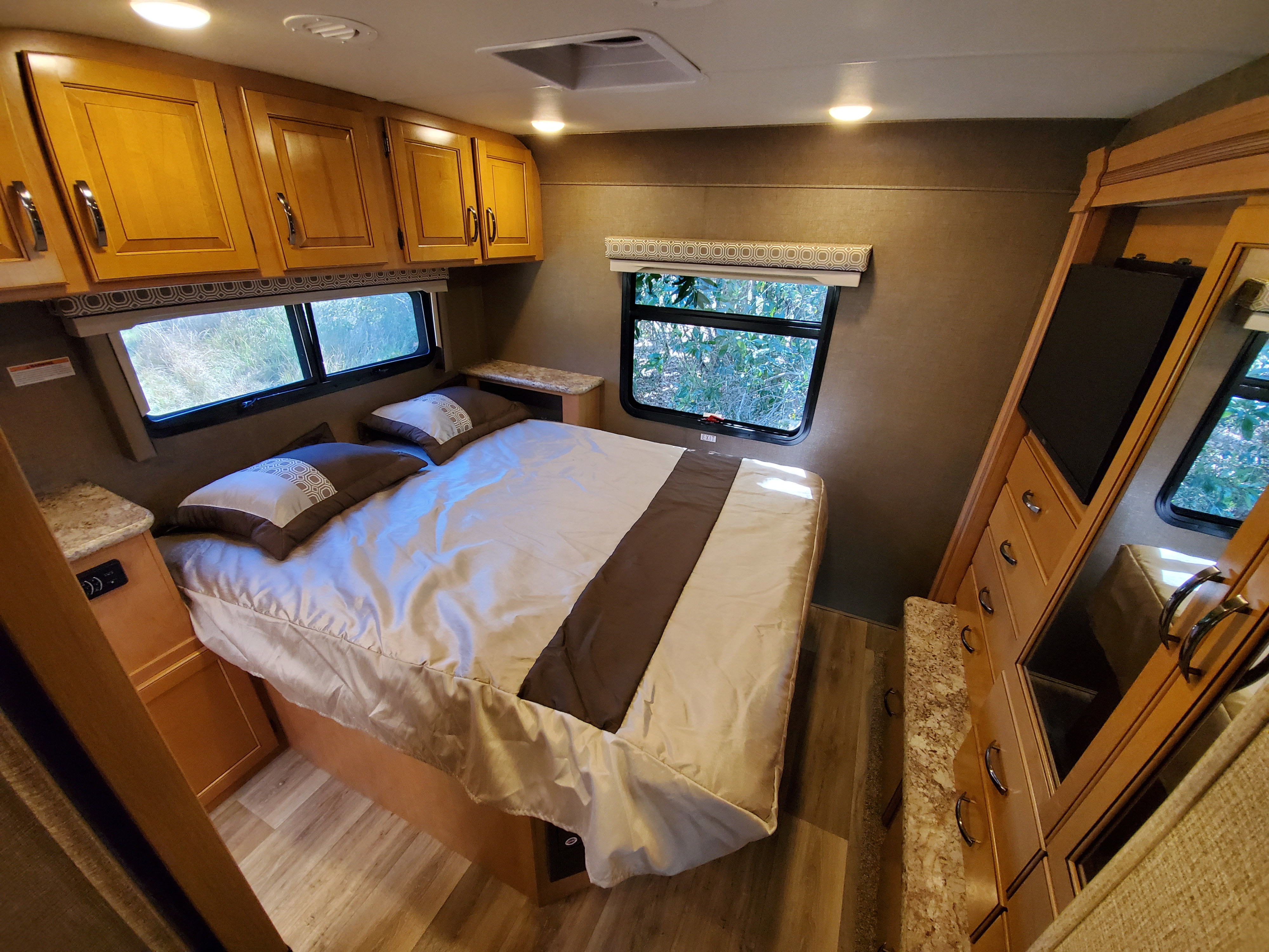Cozy RV rental bedroom featuring a comfortable bed, overhead storage, and windows overlooking nature.. Thor Motor Coach FourWinds 2017