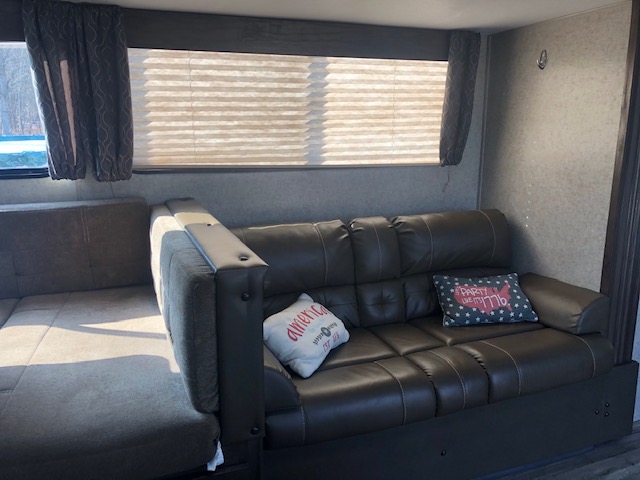 Spacious RV rental living area featuring a comfy sofa, convertible dinette, and windows with blinds.. Forest River Cherokee Grey Wolf 2019