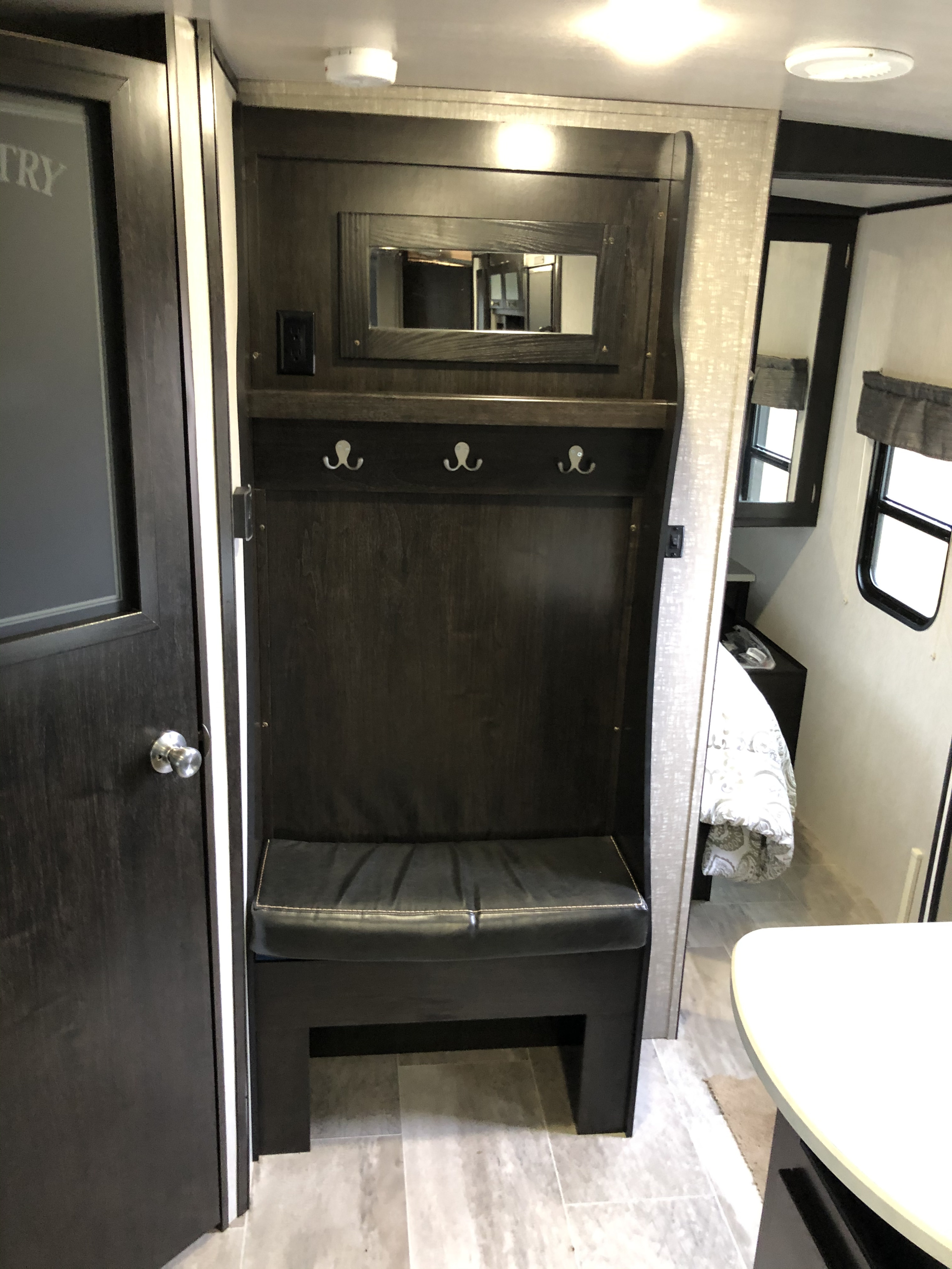 This compact RV rental features a dark wood built-in entryway: bench, hooks, and mirror. It leads to the bedroom area for organized living.. Heartland North Trail 2019