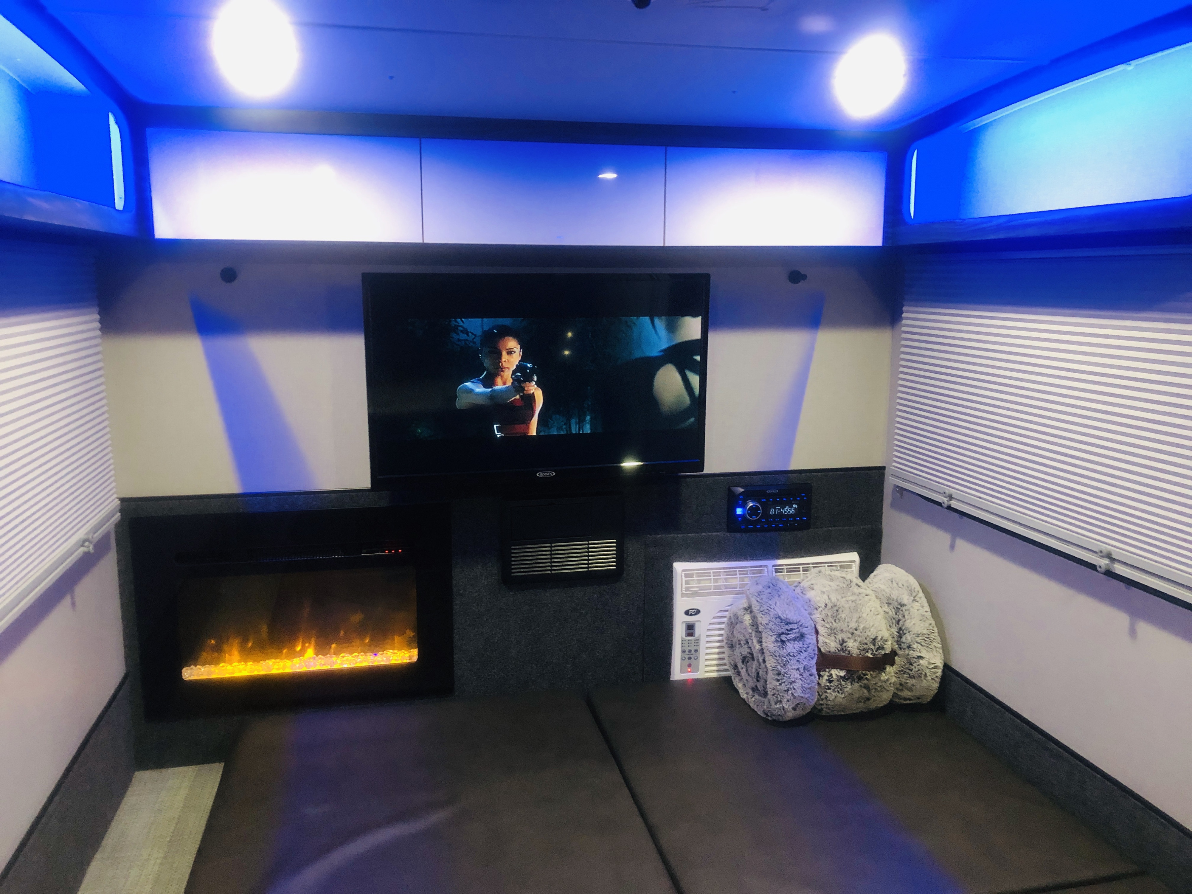 An RV rental's cozy interior, featuring a TV, electric fireplace, AC unit, and soft bedding, all illuminated by cool blue lights.. InTech RV InTech RV Trailer 2021