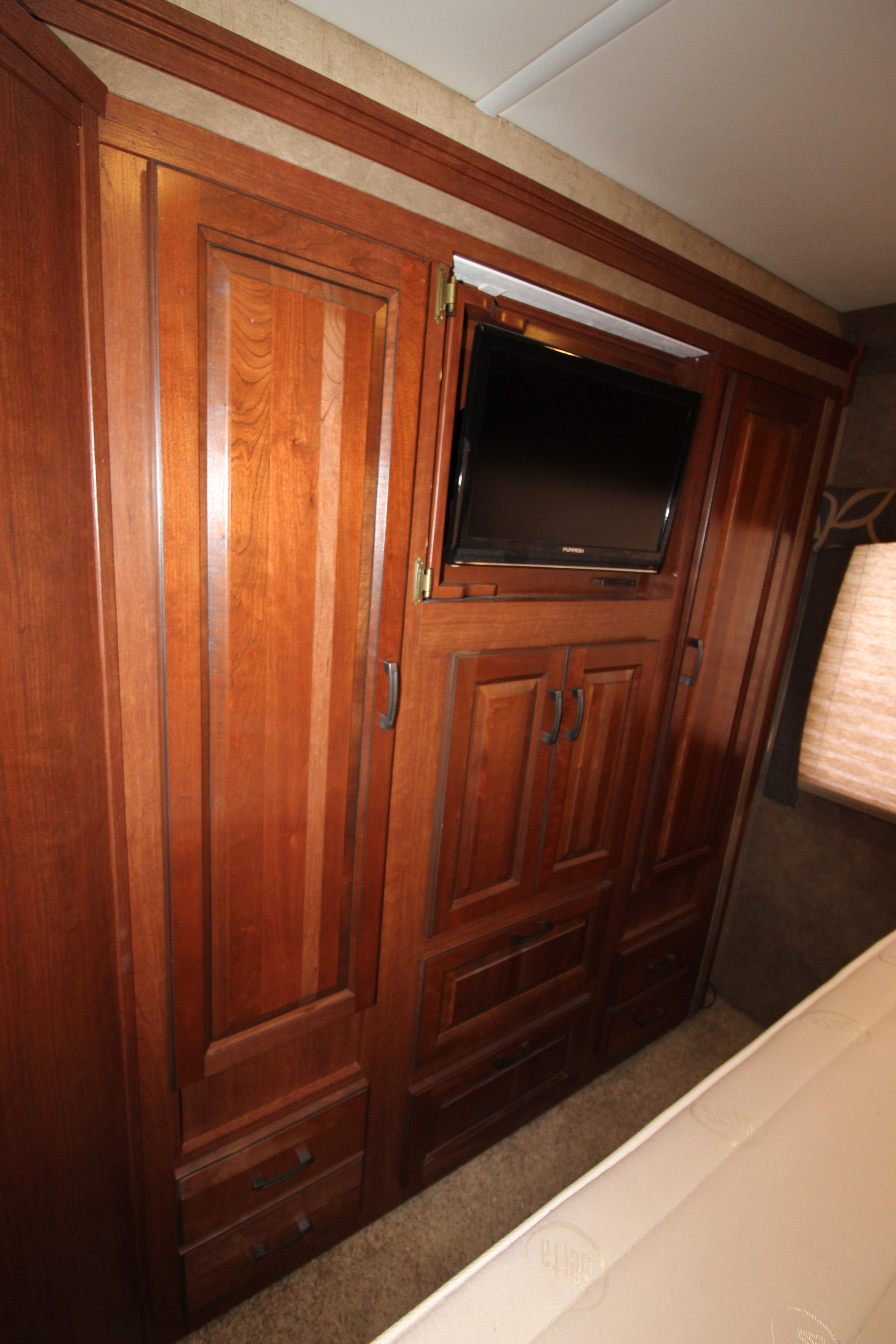 Spacious RV rental bedroom featuring extensive dark wood cabinetry, a mounted TV, ample storage drawers, and a mattress.. Forest River Forester 2016
