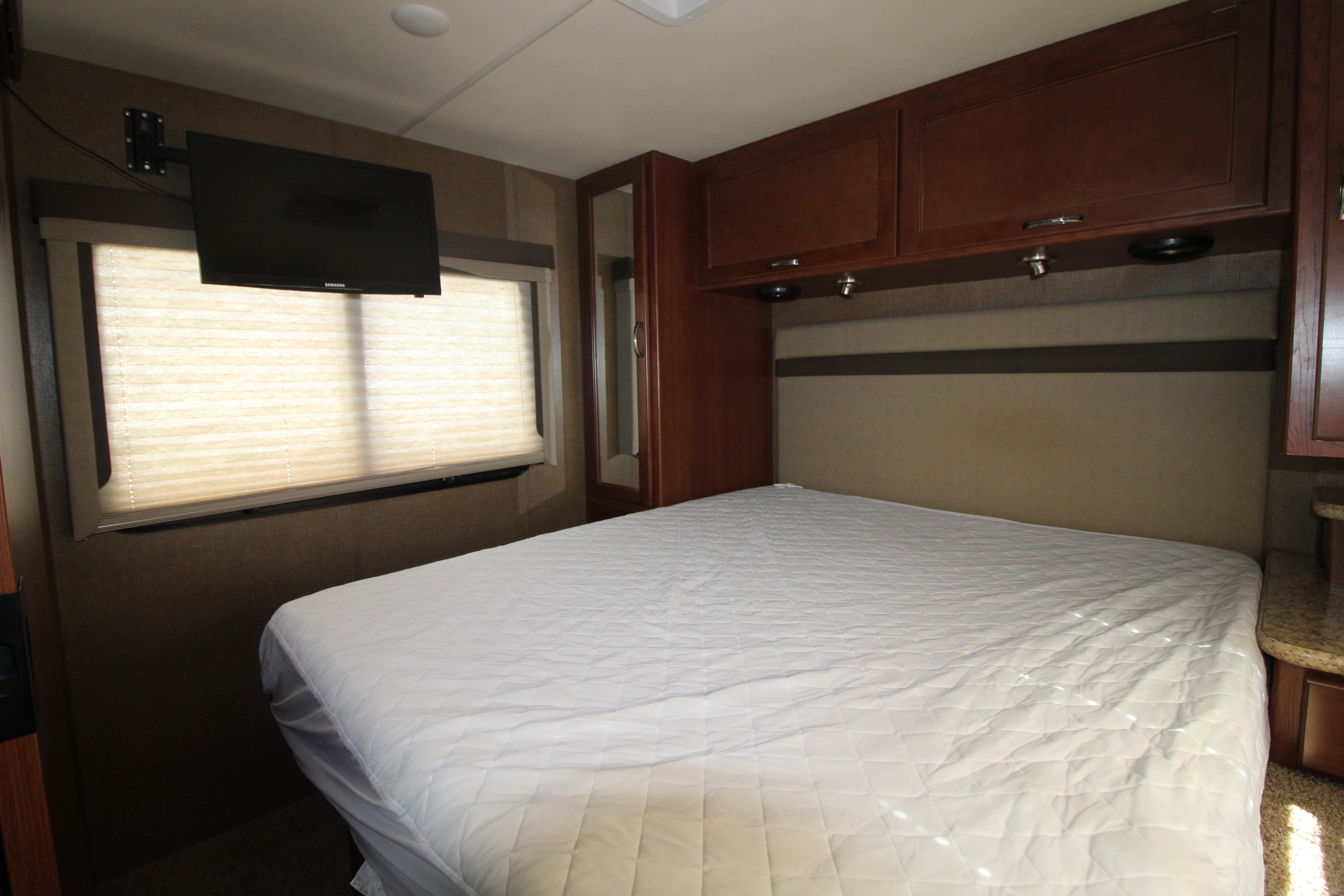 Comfortable RV rental bedroom features a queen bed with white topper, TV, and overhead storage.. Thor Motor Coach A.C.E 2016