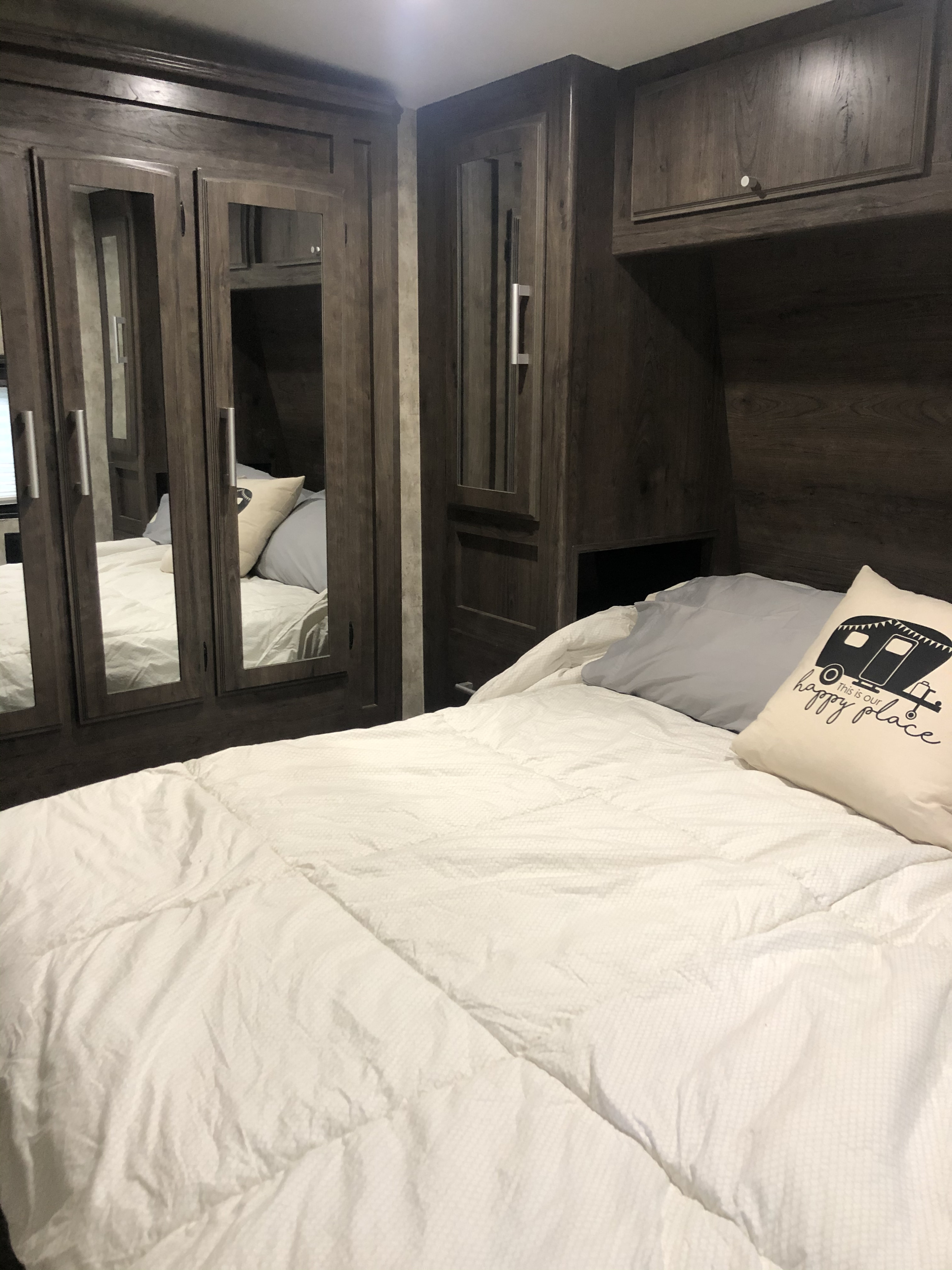 Cozy RV rental bedroom with dark wood cabinets, mirrored doors, and white bedding. A 'happy place' pillow rests on the bed.. Eclipse Recreational Vehicles Attitude2814 2019