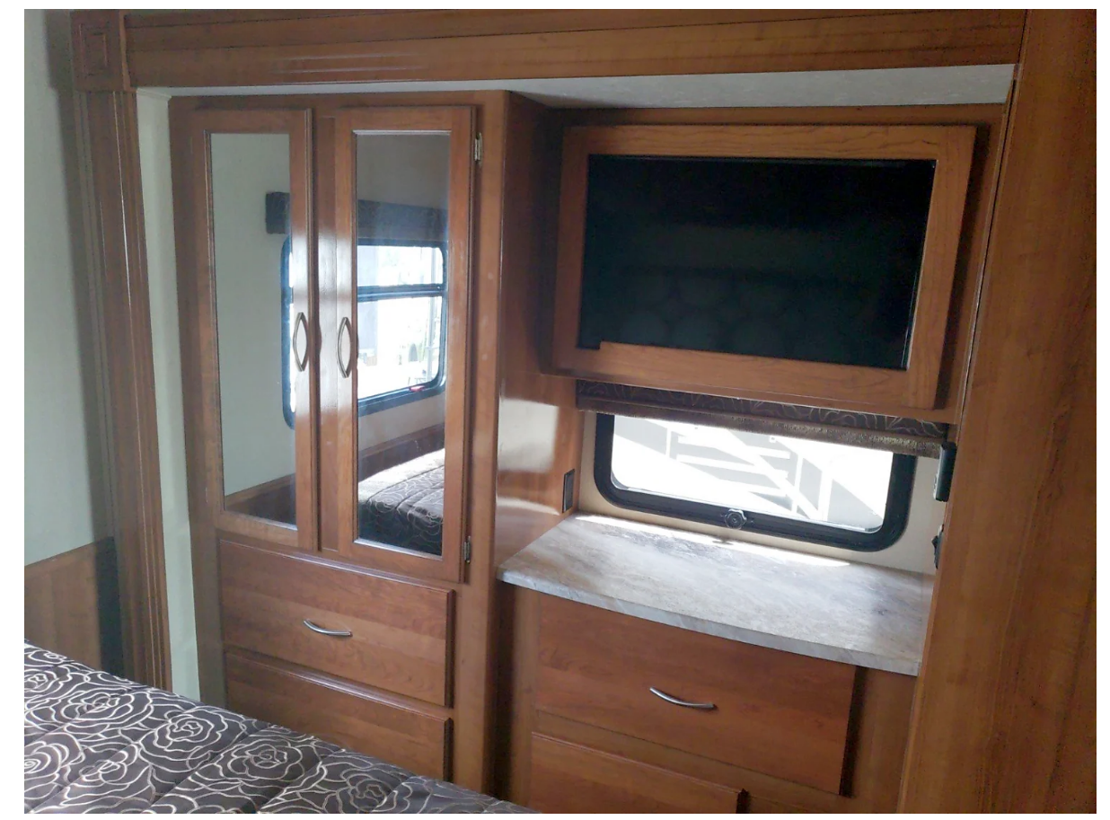 RV rental bedroom: wooden cabinets with mirrored doors, TV, window, and a bed with a patterned comforter.. Forest River Pursuit 2019