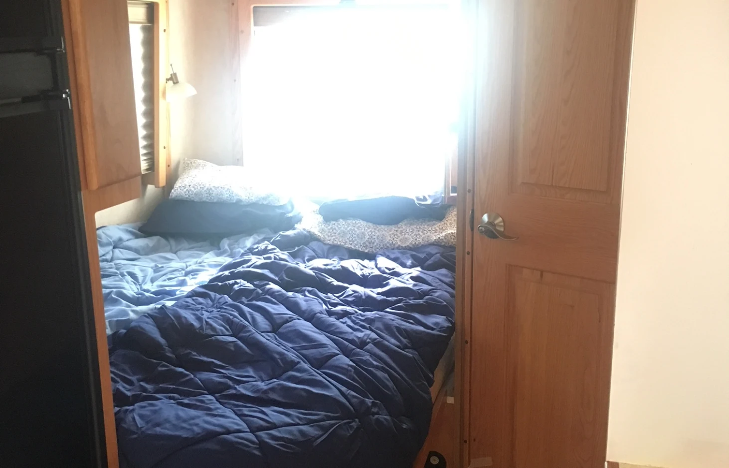 Cozy RV rental bedroom with a bed, bright natural light from the window, and wooden interior.. Born Free Born Free Motorhome 2005