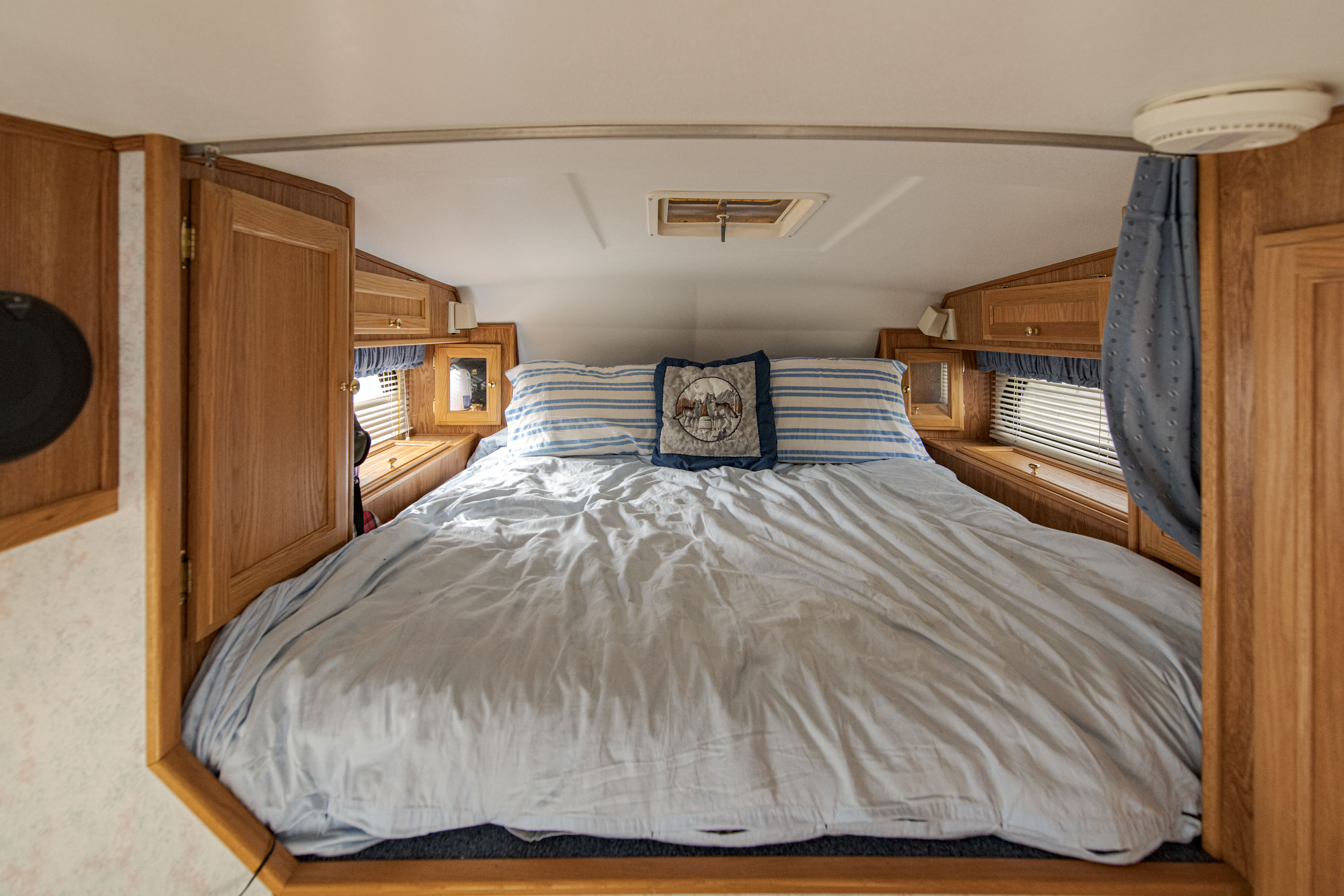 This RV rental's cozy bedroom features a large bed with light blue bedding, decorative pillows, and wooden cabinetry.. Ford Other 1996