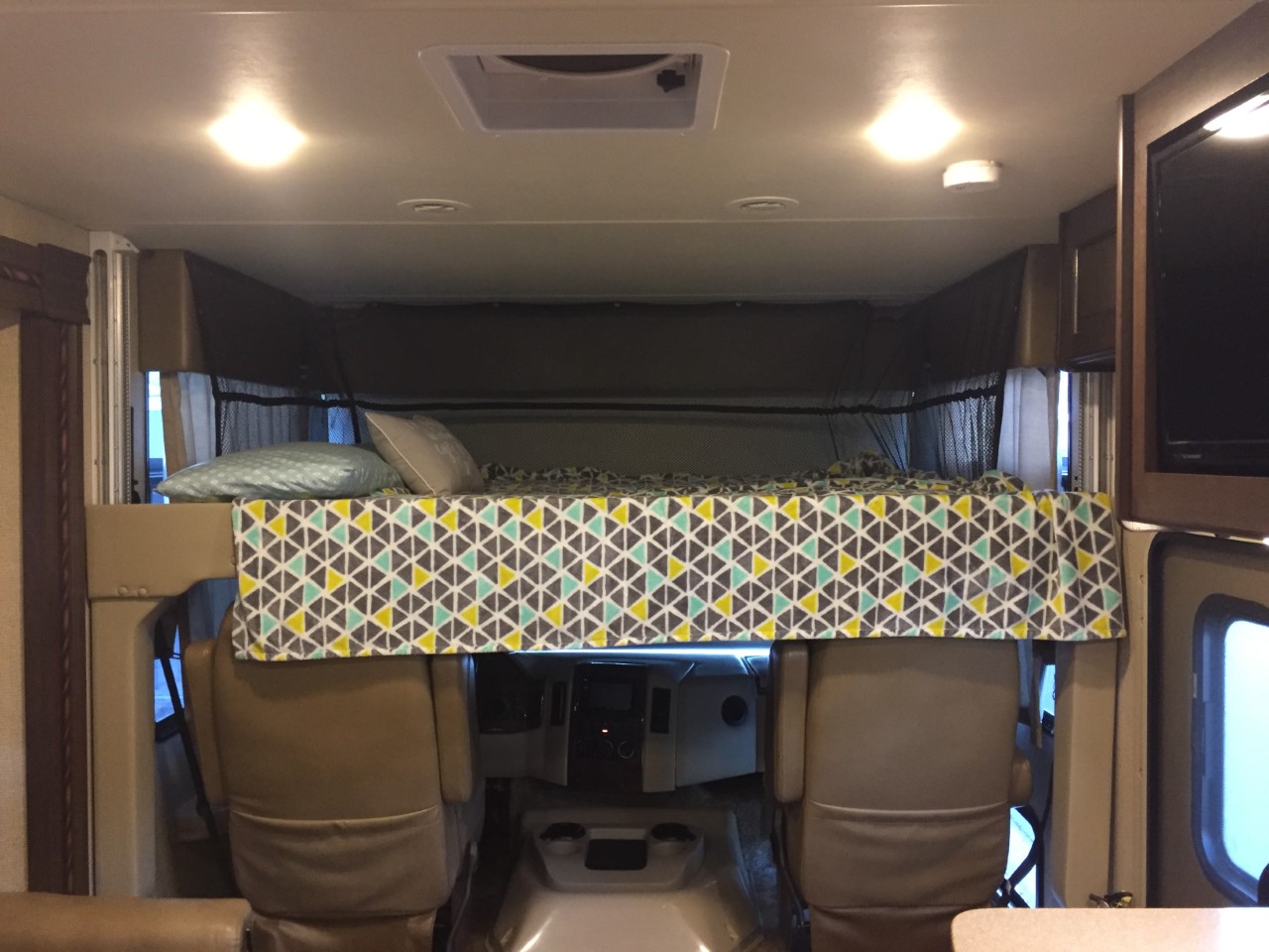 Inside an RV rental: a comfortable cab-over bunk bed with patterned bedding sits above the cockpit seats.. Thor Windsport 2017