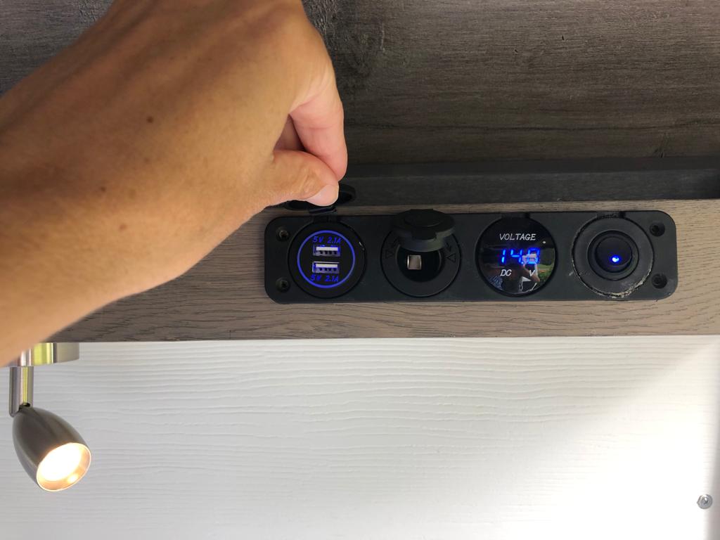 Hand on an RV rental's interior power panel, showing USB charging, a 12V socket, and a 14.8V DC voltage display.. Dodge Sprinter 2500 170ext 2015