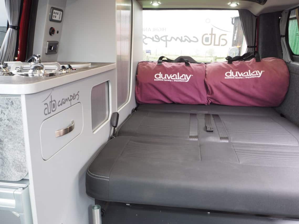 Alto campers RV rental interior: a compact kitchen & comfy fold-out bed with 'duvalay' bedding, perfect for road trips.. Ford Transit Custom 2+2 berth Pop Top, manual 2020