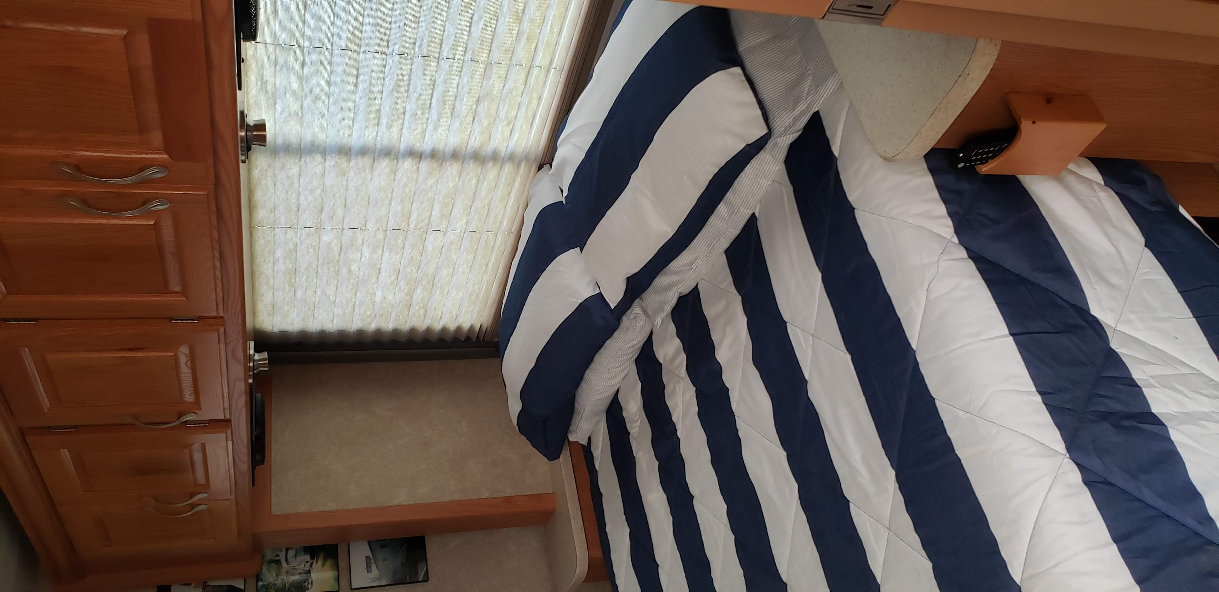 Inside an RV rental bedroom: blue/white striped comforter, warm wood cabinets, and pleated window blinds.. Thor Motor Coach Hurricane 34N 2006