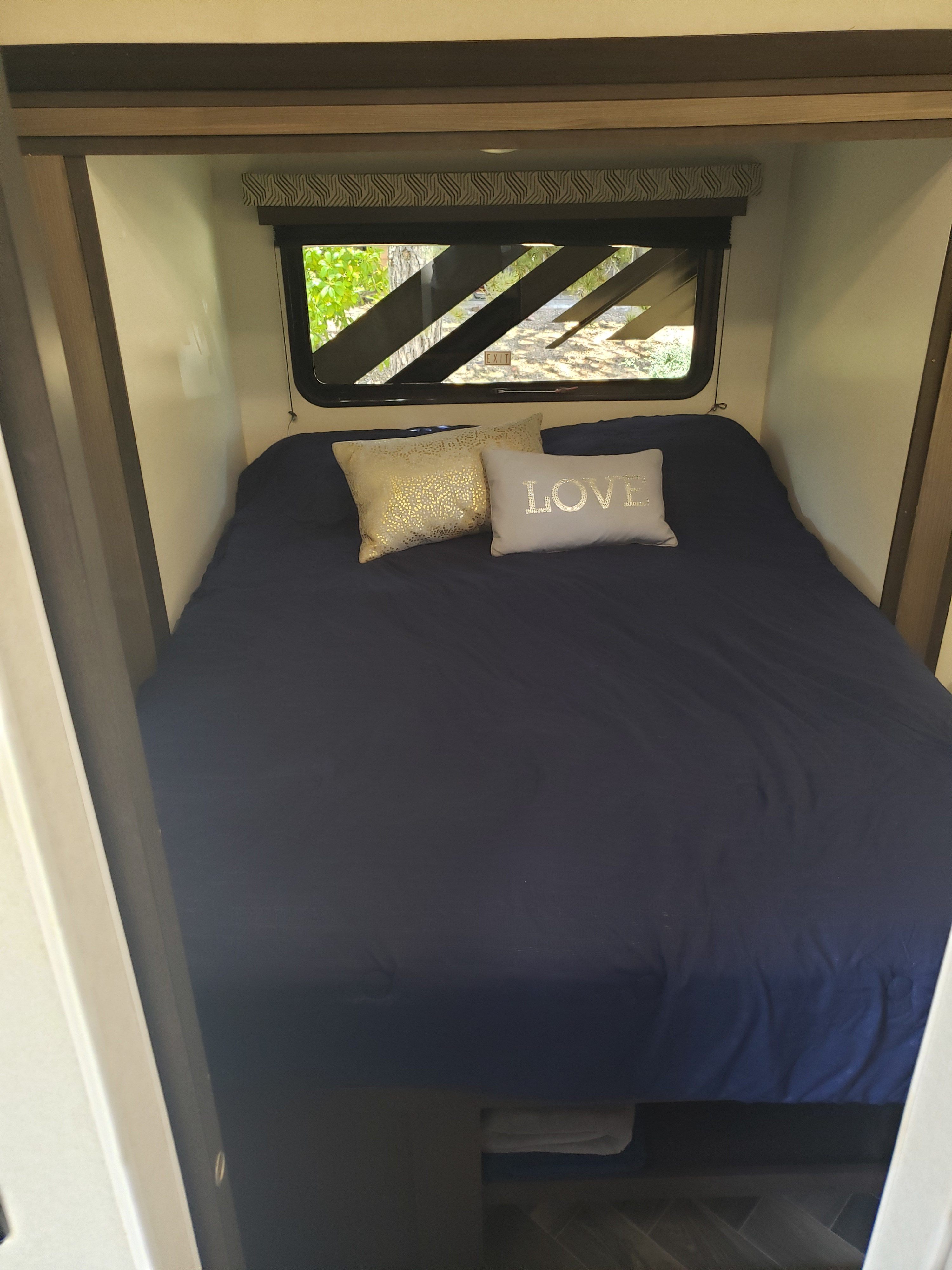 Relax in this cozy RV rental bedroom. Features a dark blue bed, "LOVE" pillow, and window view.. Forest River Stealth 2019