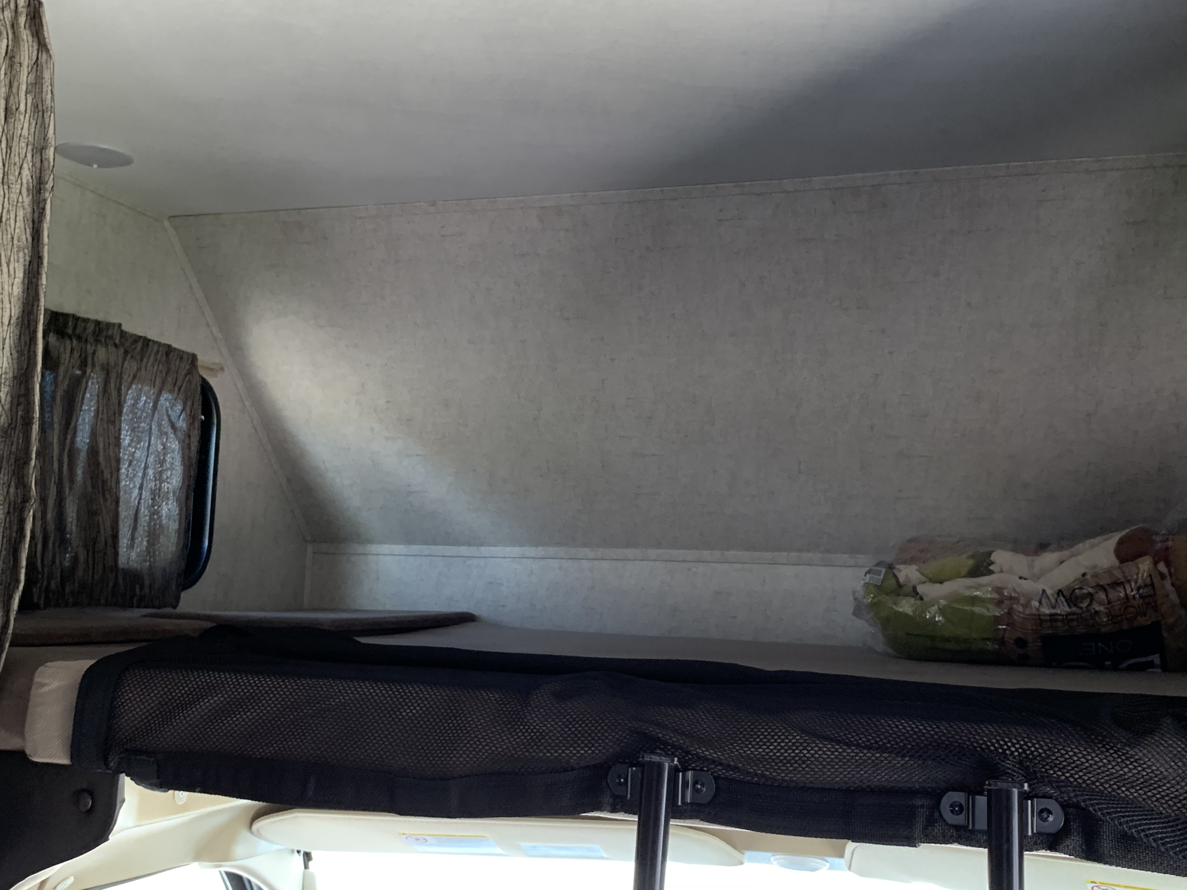 Overhead sleeping area in an RV rental, featuring a safety net and window curtain.. Forest River Sunseeker 2019